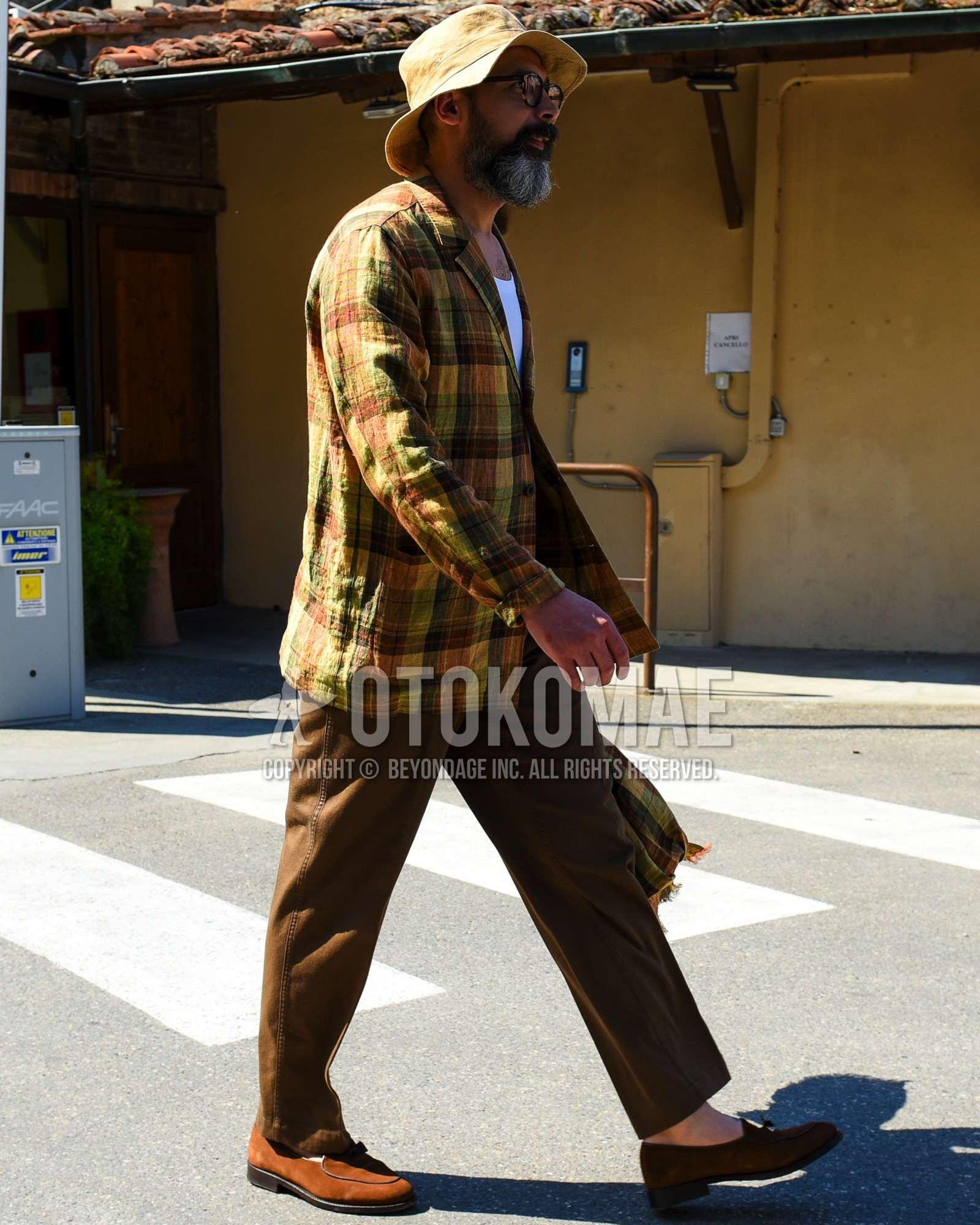 Men's spring summer outfit with beige plain bucket hat, brown tortoiseshell glasses, yellow orange check tailored jacket, white plain t-shirt, brown plain cotton pants, brown tassel loafers leather shoes, brown suede shoes leather shoes.