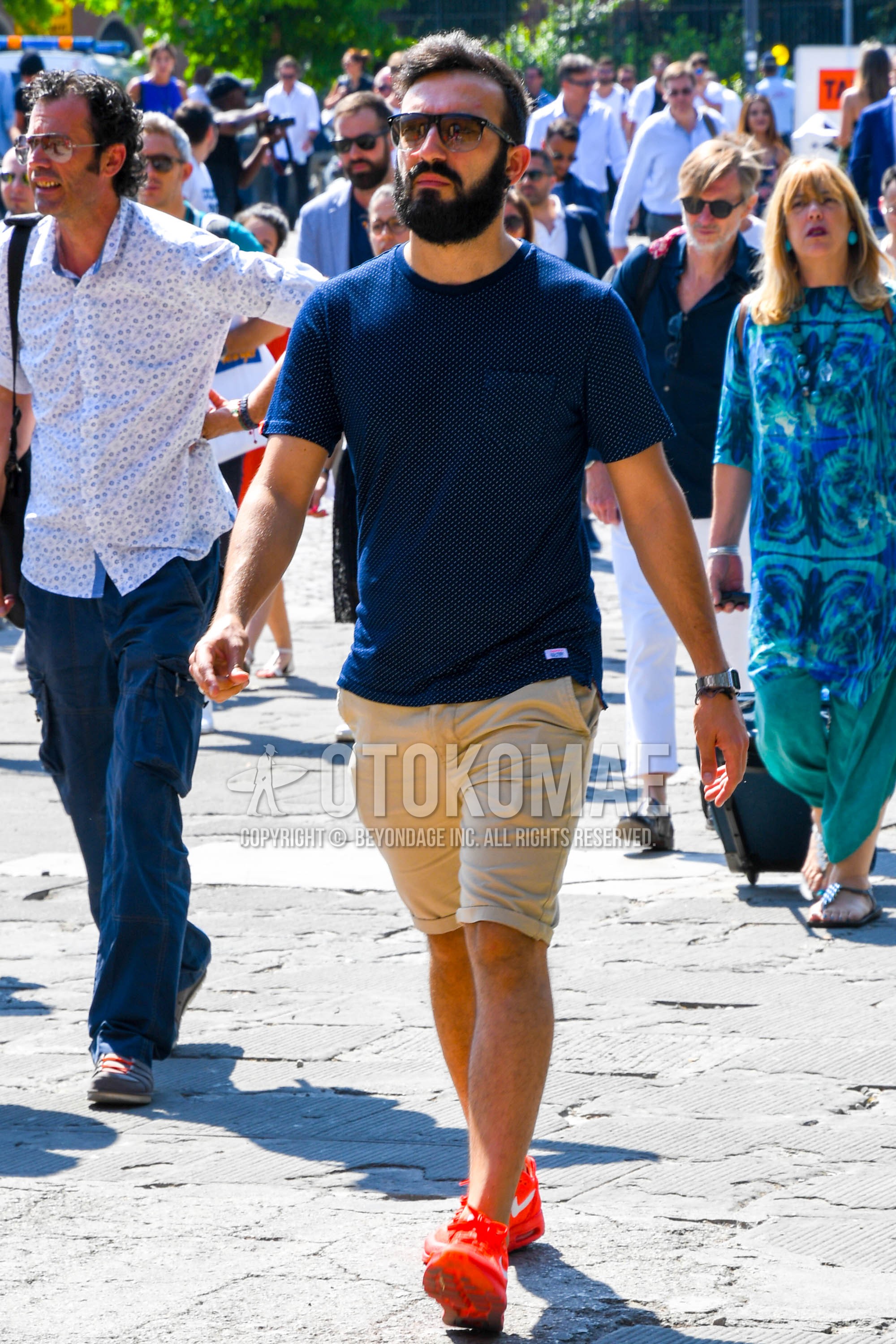 Men's summer outfit with plain sunglasses, navy t-shirt, beige plain short pants, orange low-cut sneakers.