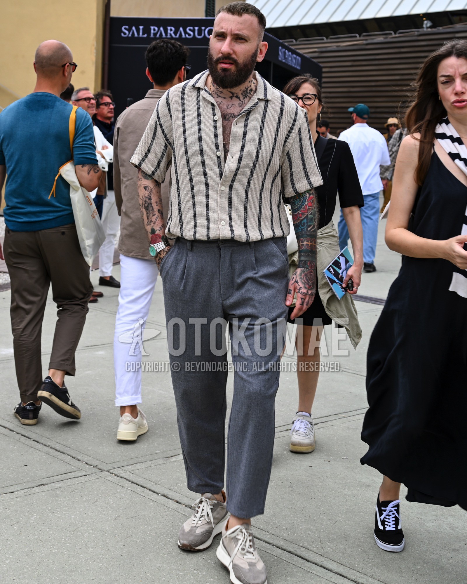 Men's spring summer outfit with beige stripes polo shirt, gray plain slacks, gray plain pleated pants, gray low-cut sneakers.