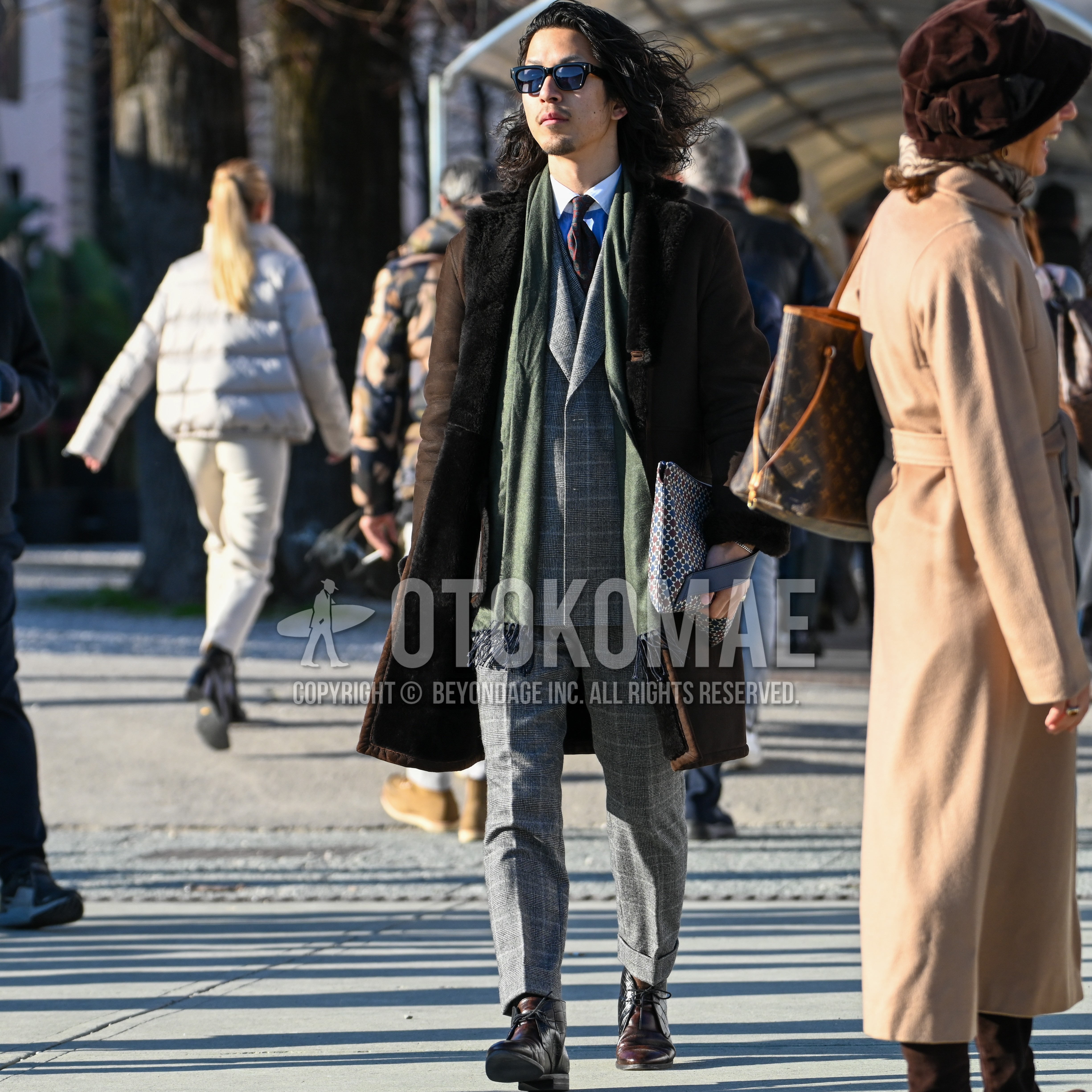 Men's autumn winter outfit with black plain sunglasses, olive green plain scarf, brown outerwear, light blue white tops/innerwear shirt, brown chukka boots, gray check three-piece suit, brown whole pattern necktie.