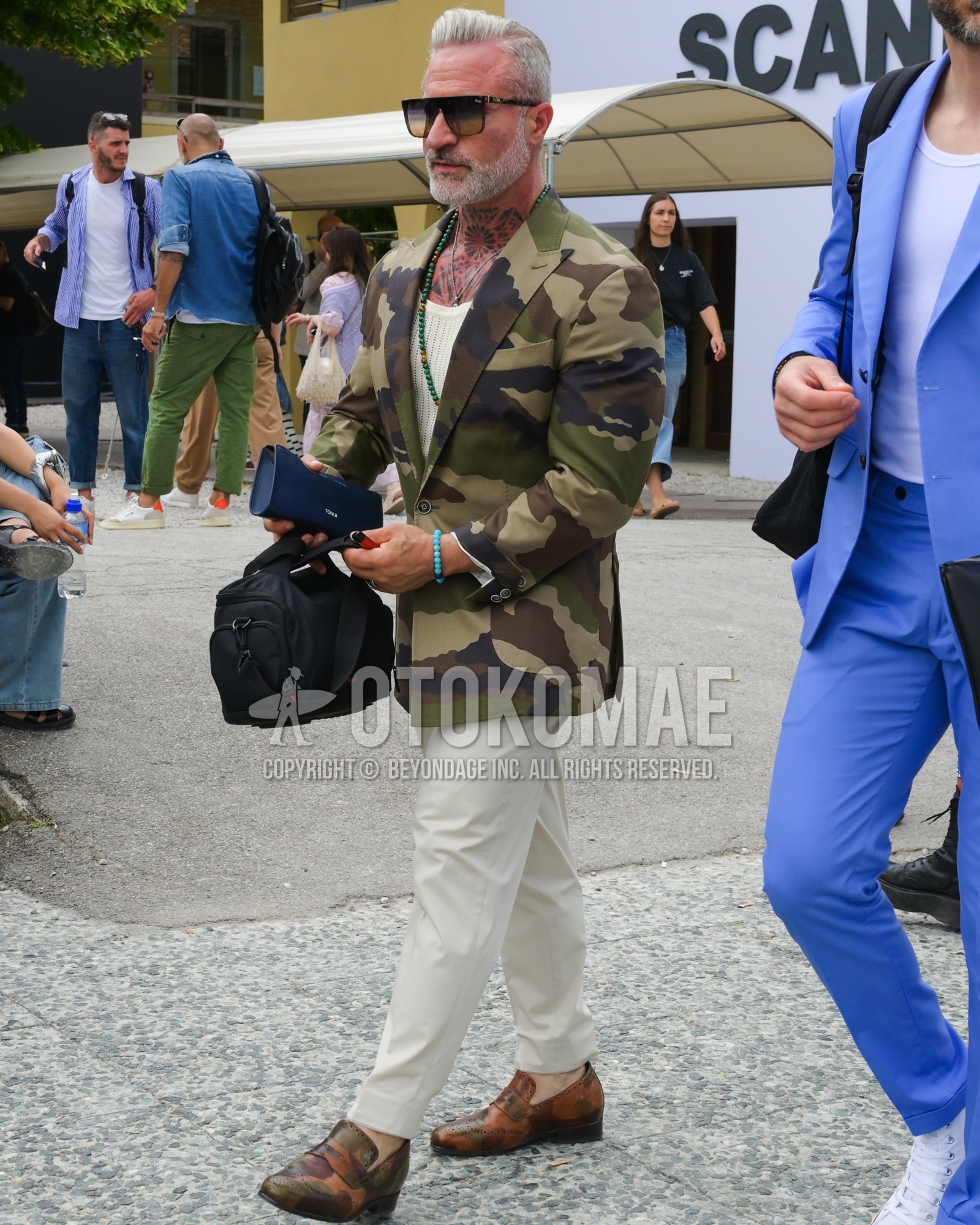 Men's spring summer autumn outfit with black plain sunglasses, multi-color olive green camouflage tailored jacket, white plain slacks, brown coin loafers leather shoes.