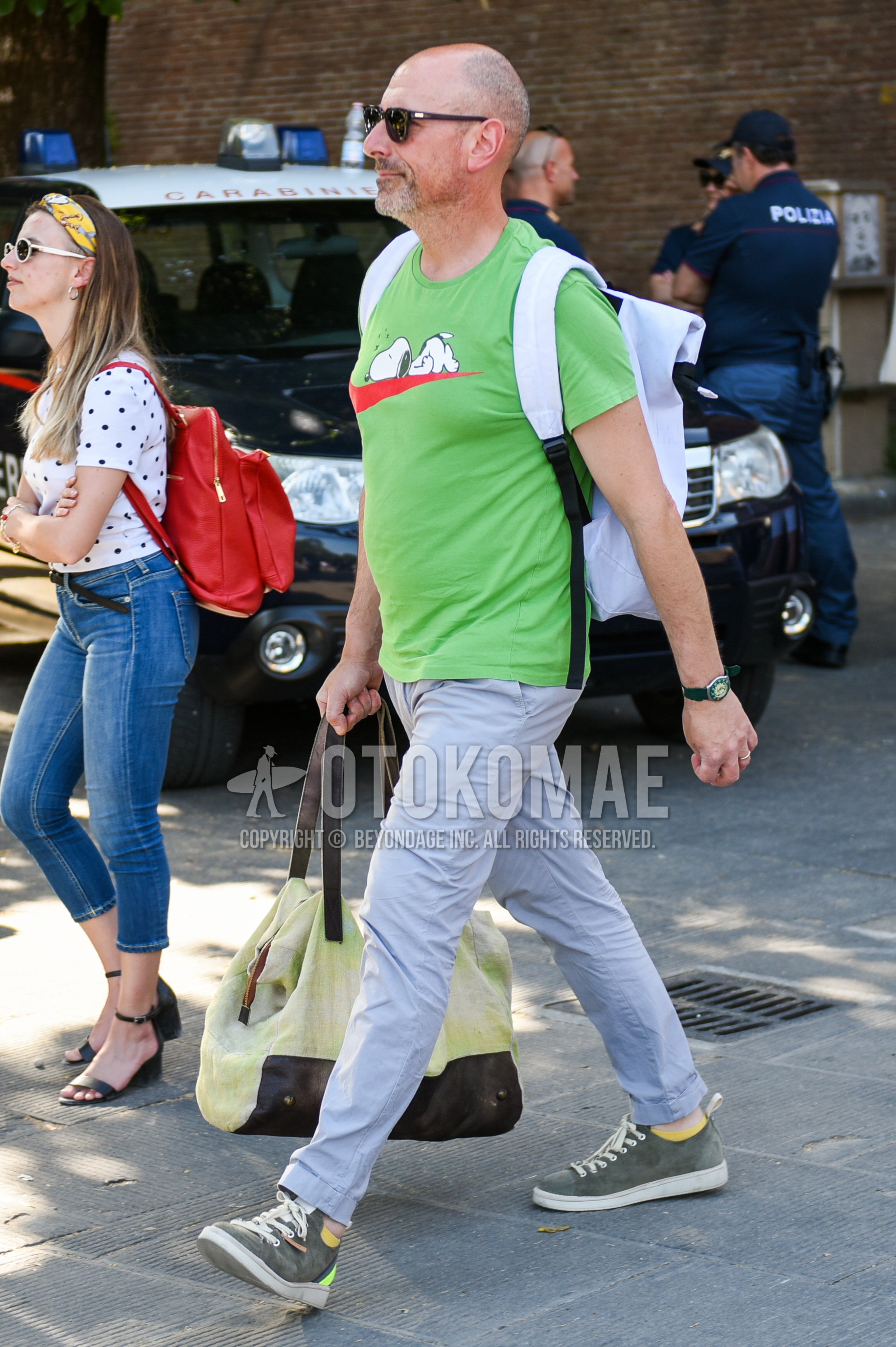 Men's summer outfit with black plain sunglasses, green deca logo t-shirt, gray plain cotton pants, gray low-cut sneakers.