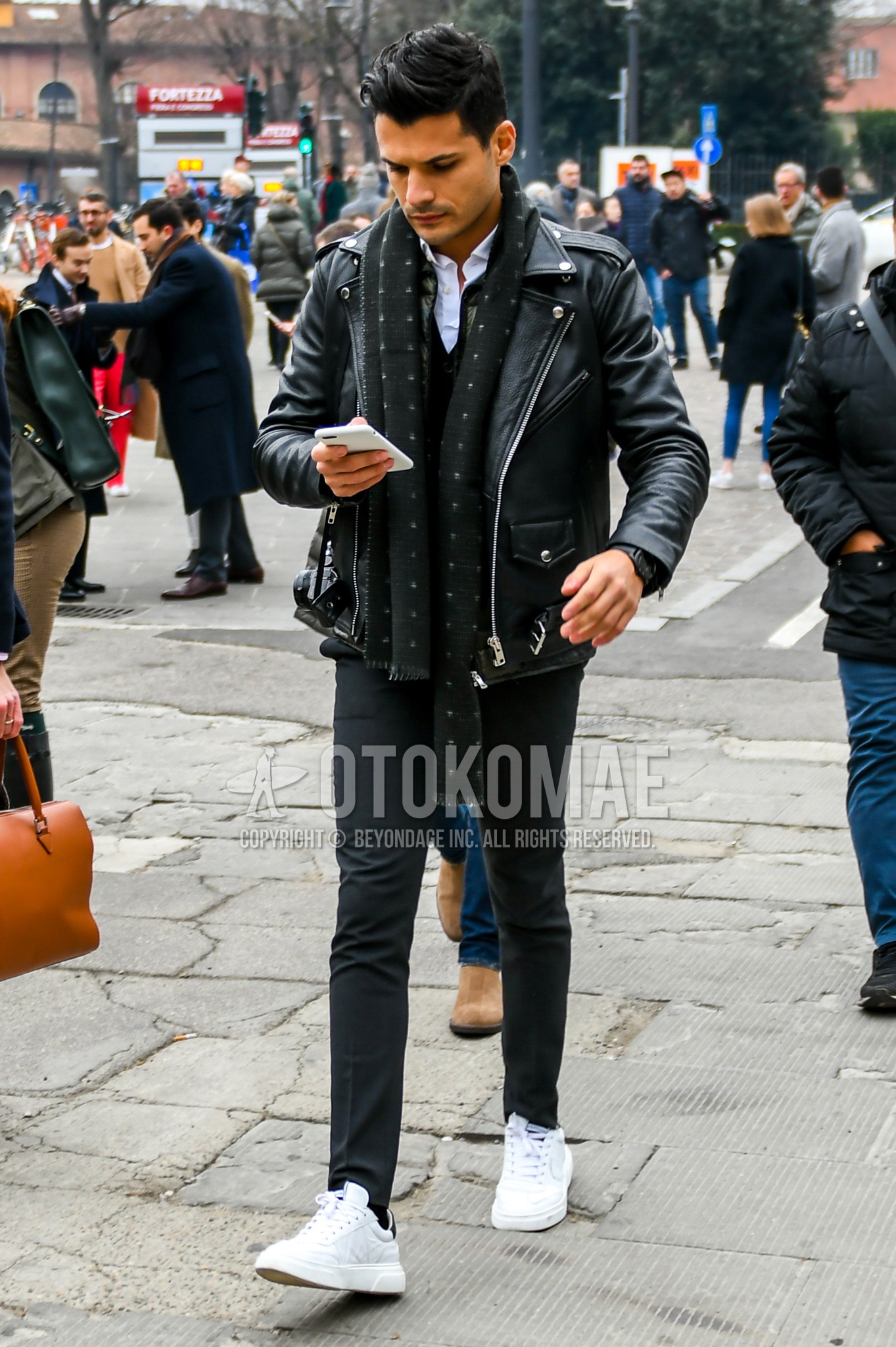 Men's winter outfit with black dots scarf, black plain riders jacket, dark gray plain skinny pants, white low-cut sneakers.