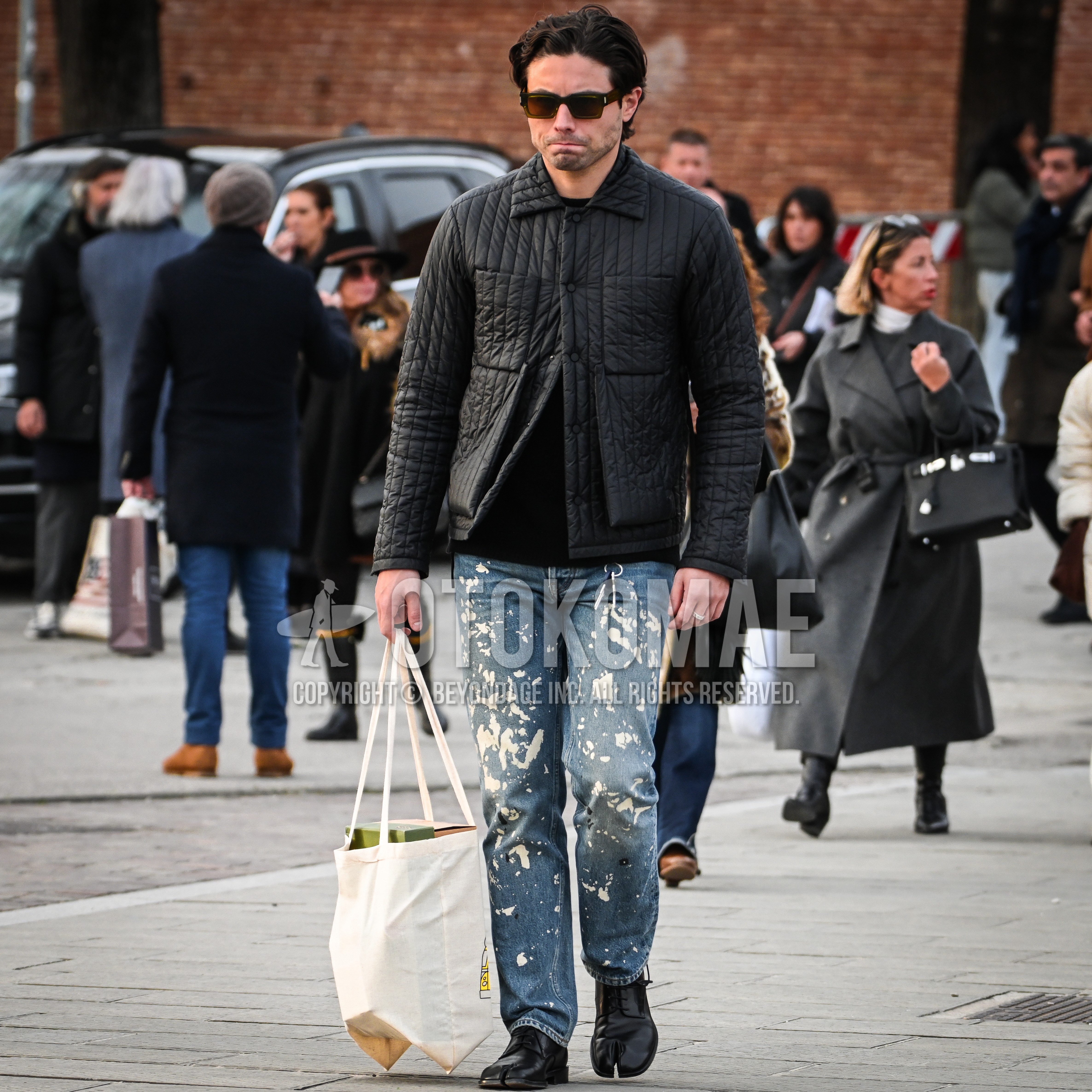 Men's autumn winter outfit with brown plain sunglasses, black plain quilted jacket, black plain sweater, bottoms damaged jeans, black  leather shoes, white bag tote bag.