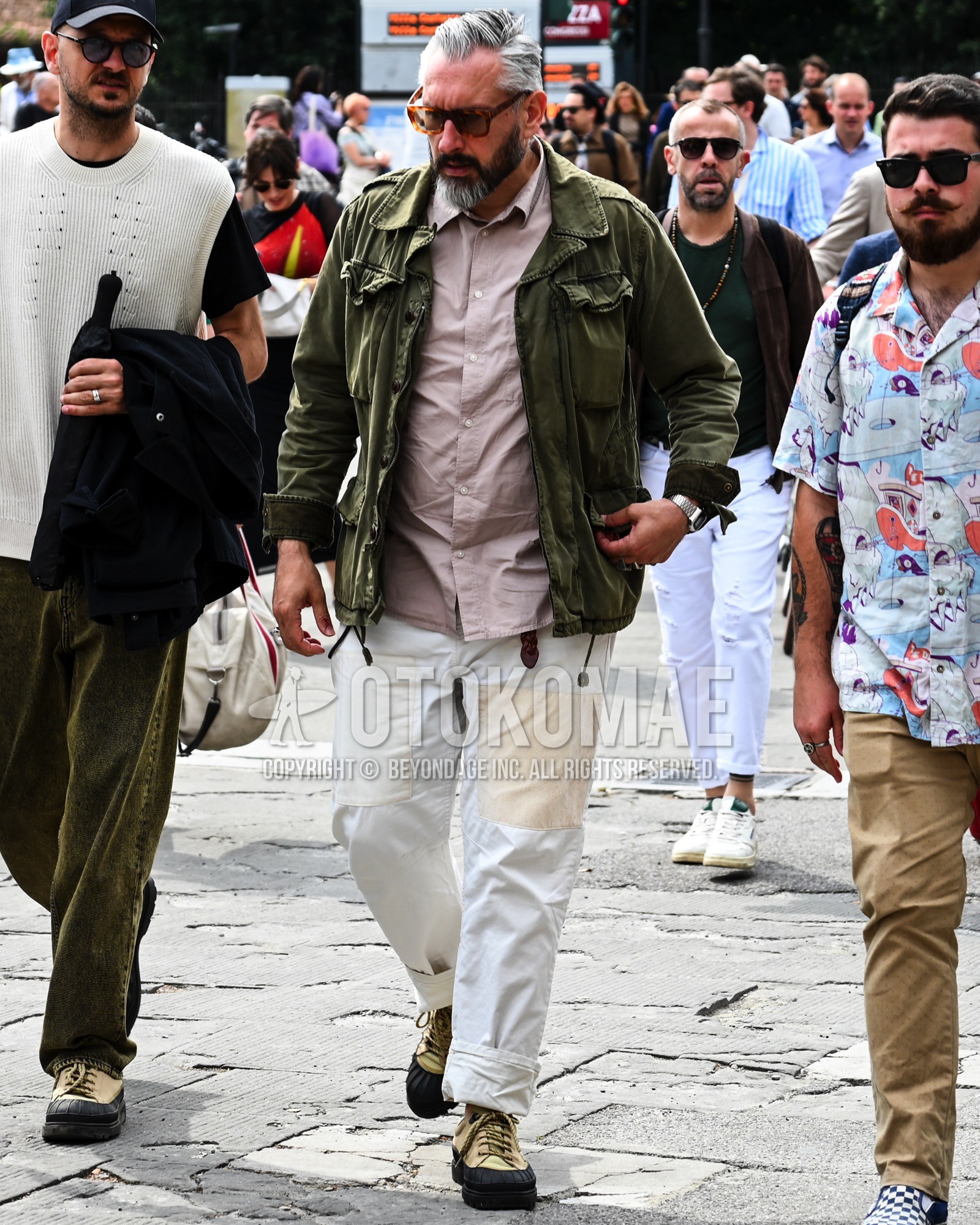 Men's spring summer autumn outfit with black tortoiseshell sunglasses, olive green plain military jacket, pink plain shirt, white plain wide pants, beige low-cut sneakers.