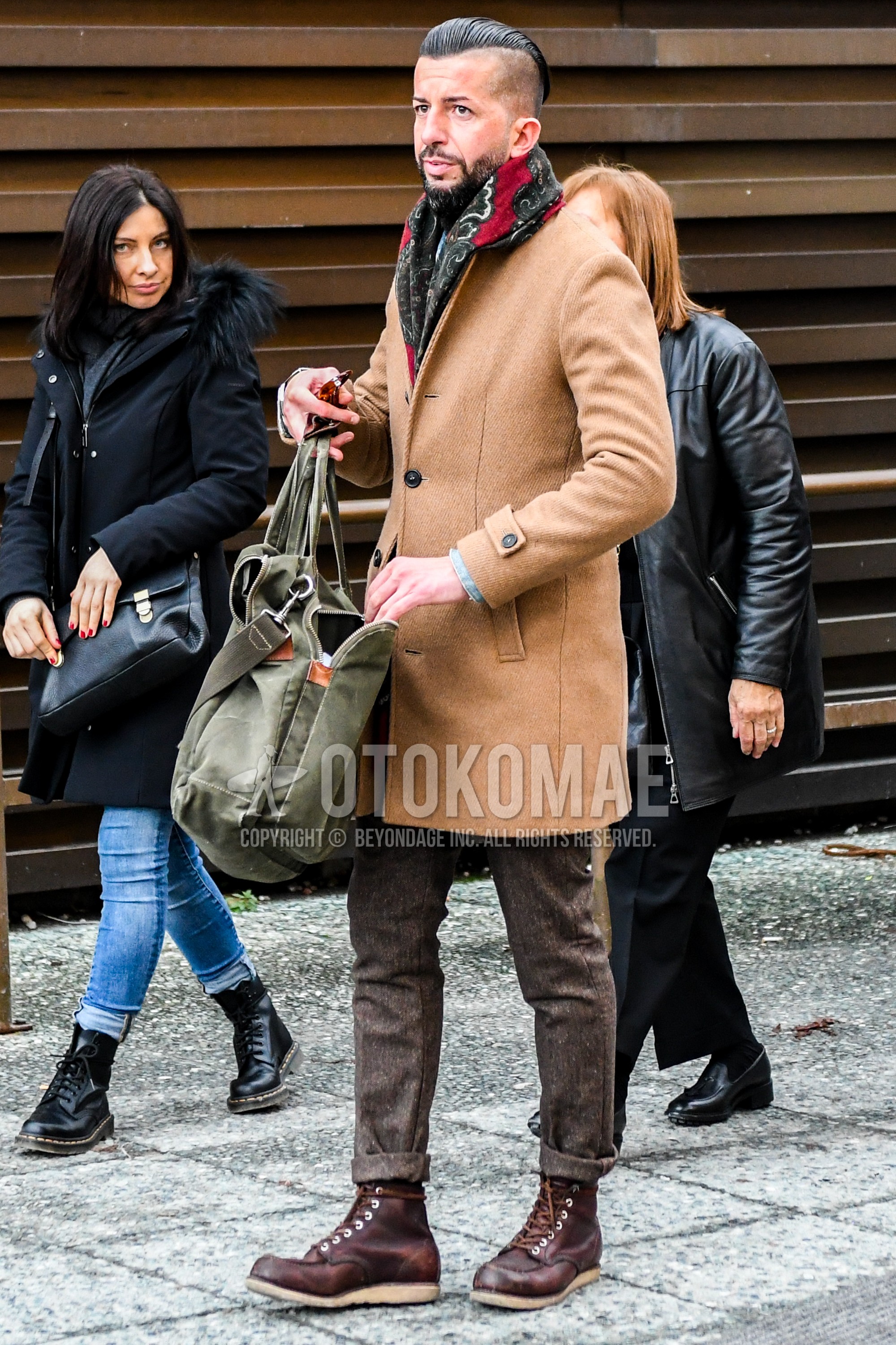 Men's winter outfit with multi-color scarf scarf, beige plain chester coat, brown plain slacks, brown work boots, olive green plain briefcase/handbag.