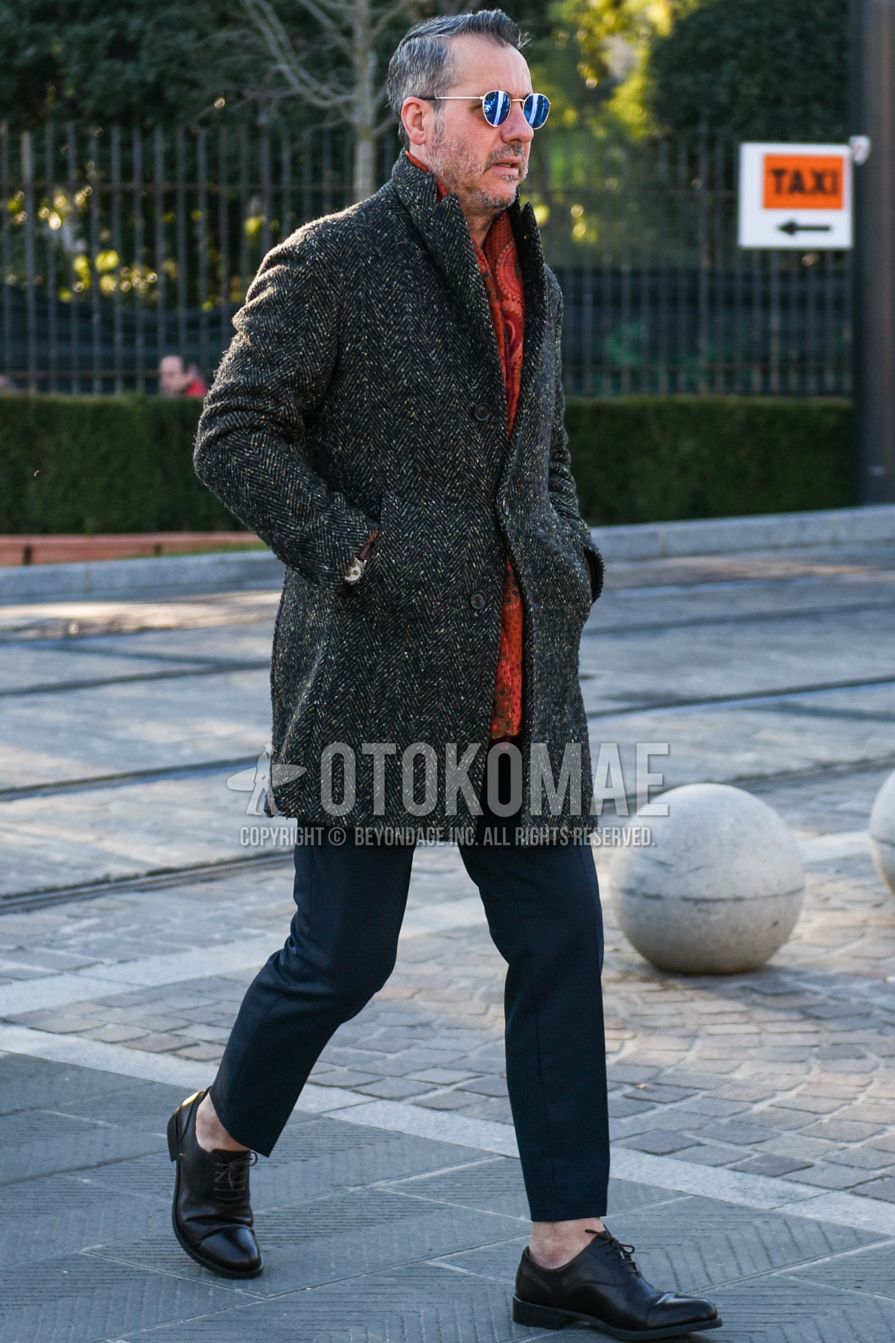 Men's autumn winter outfit with gold plain sunglasses, orange scarf scarf, gray herringbone chester coat, dark gray plain slacks, dark gray plain cropped pants, black straight-tip shoes leather shoes.