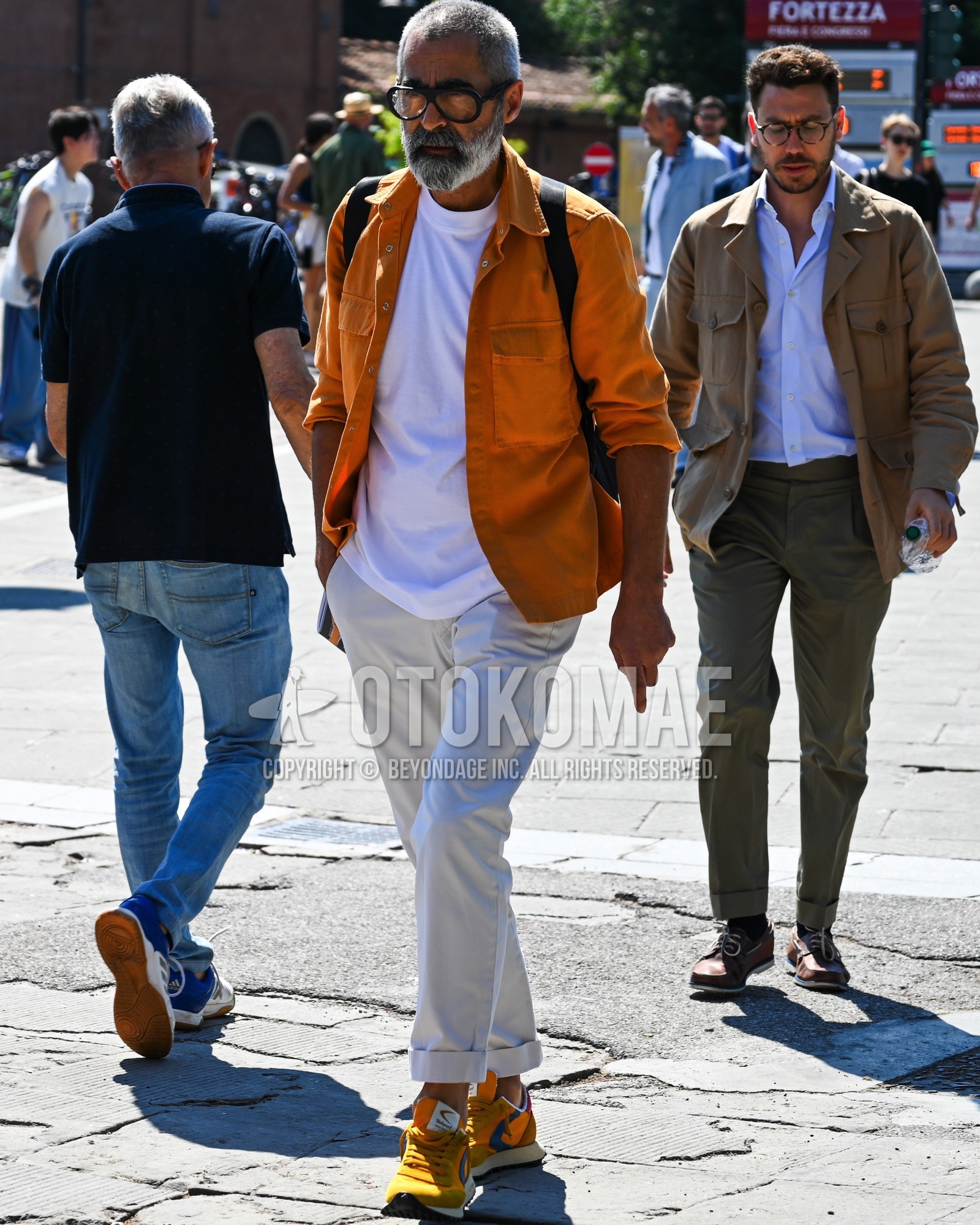 Men's spring summer autumn outfit with clear plain sunglasses, yellow plain shirt jacket, white plain t-shirt, white plain chinos, yellow low-cut sneakers.