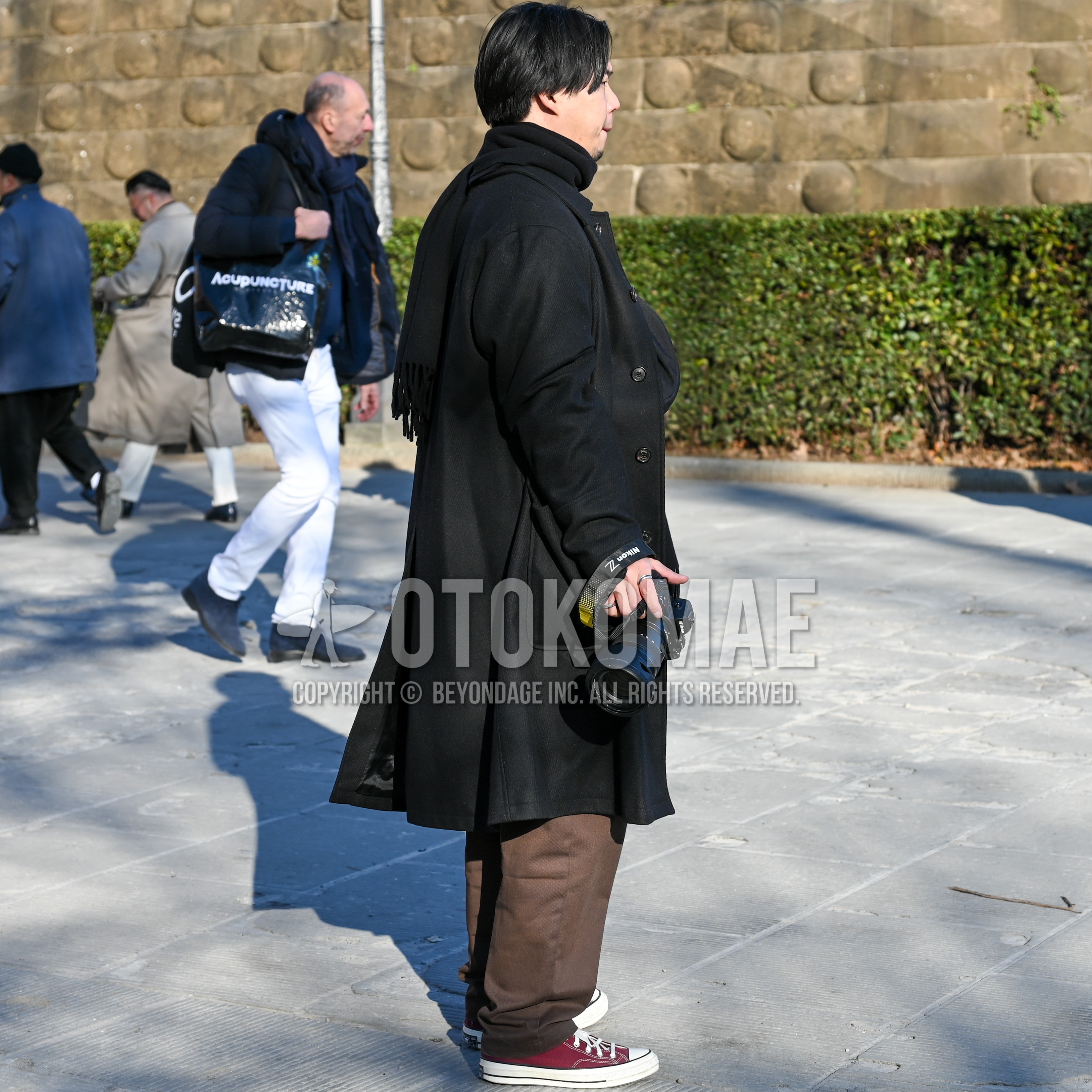 Men's autumn winter outfit with black plain scarf, black plain stenkarrer coat, brown plain wide pants, red low-cut sneakers.
