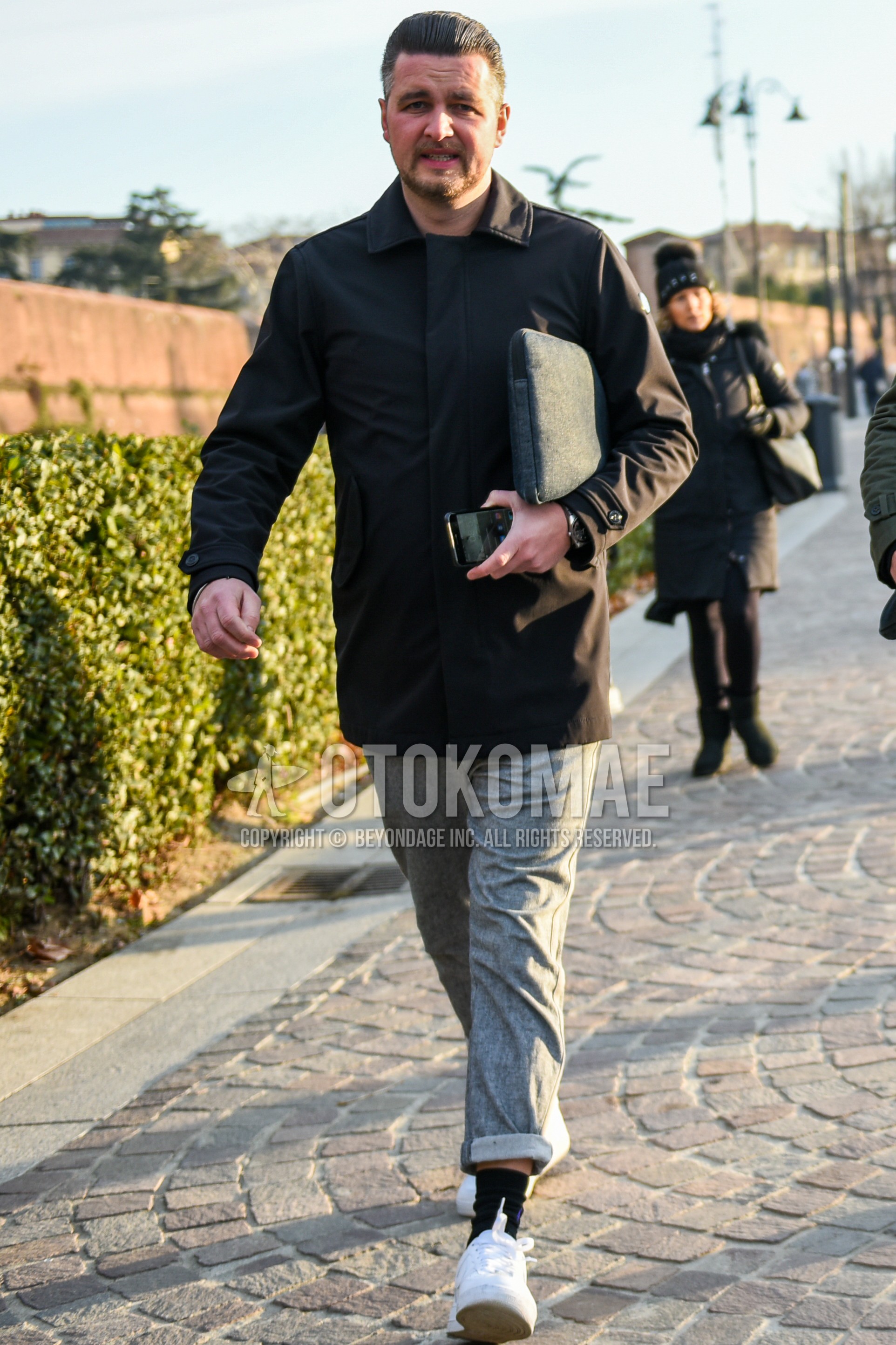 Men's autumn winter outfit with black plain stenkarrer coat, gray plain slacks, black plain socks, white low-cut sneakers, gray plain clutch bag/second bag/drawstring bag.