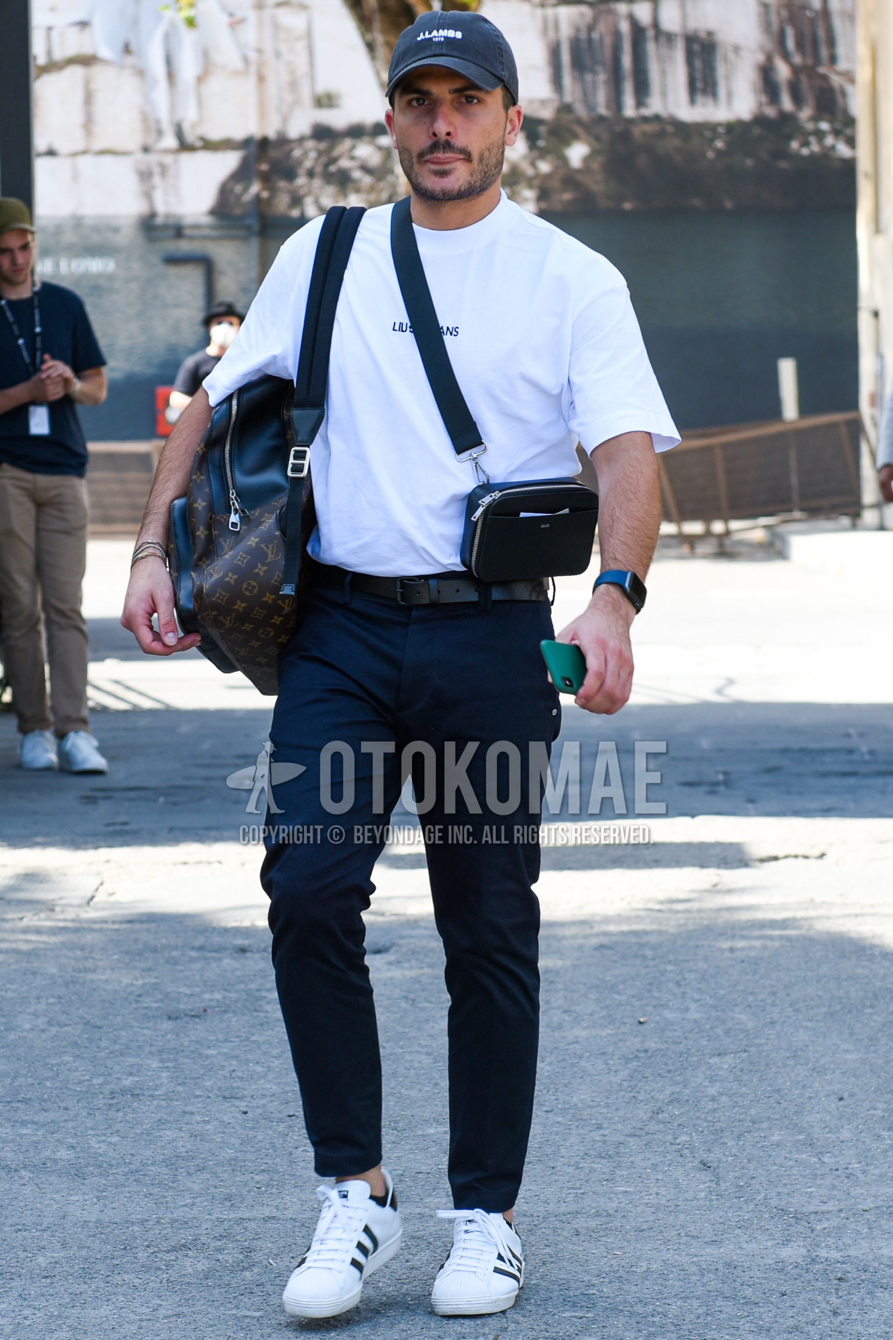 Men's spring summer outfit with dark gray one point baseball cap, white one point t-shirt, black plain leather belt, navy plain chinos, white low-cut sneakers, brown bag backpack, black plain succoshe.