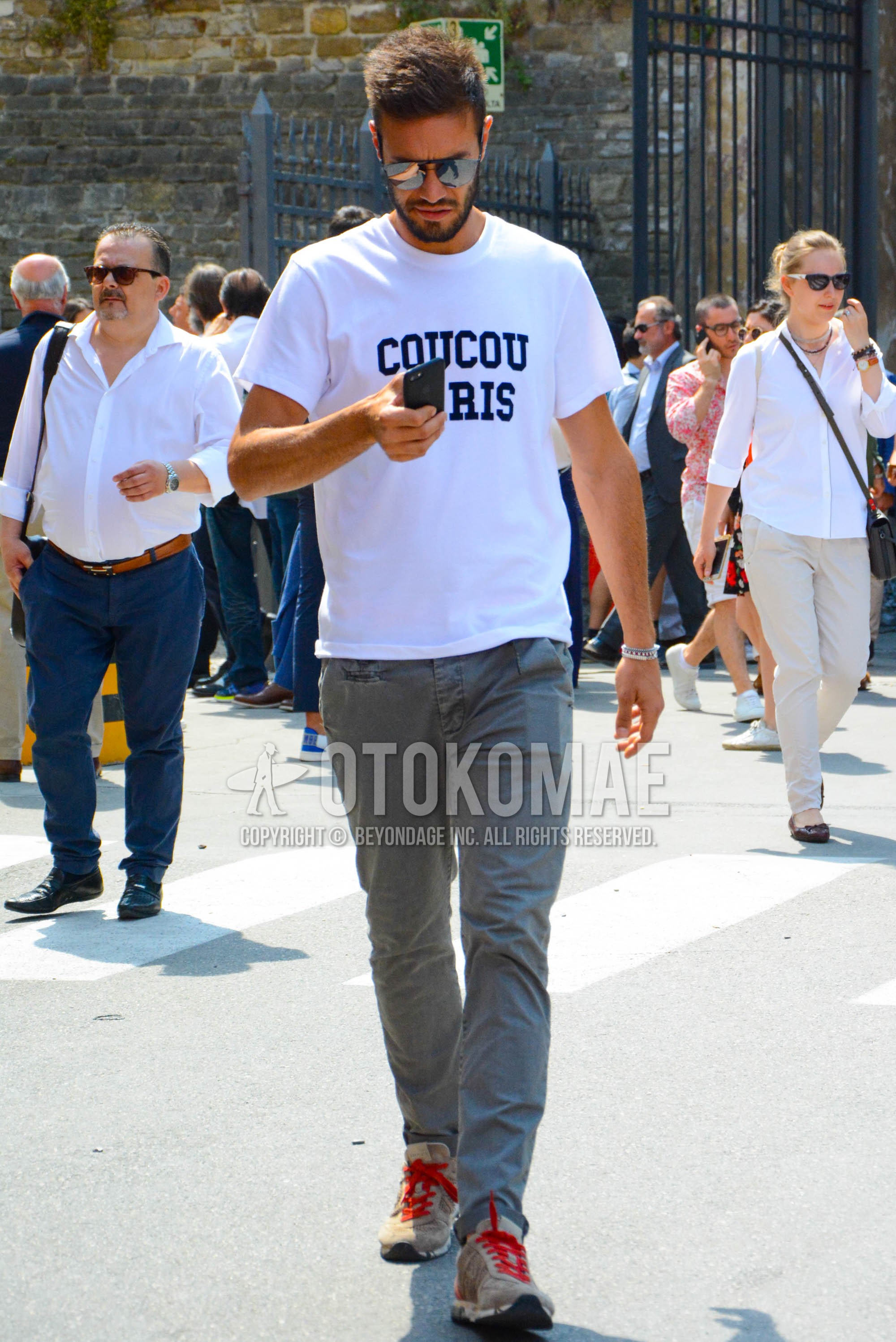 Men's spring summer outfit with silver plain sunglasses, white graphic t-shirt, gray plain chinos, beige low-cut sneakers.
