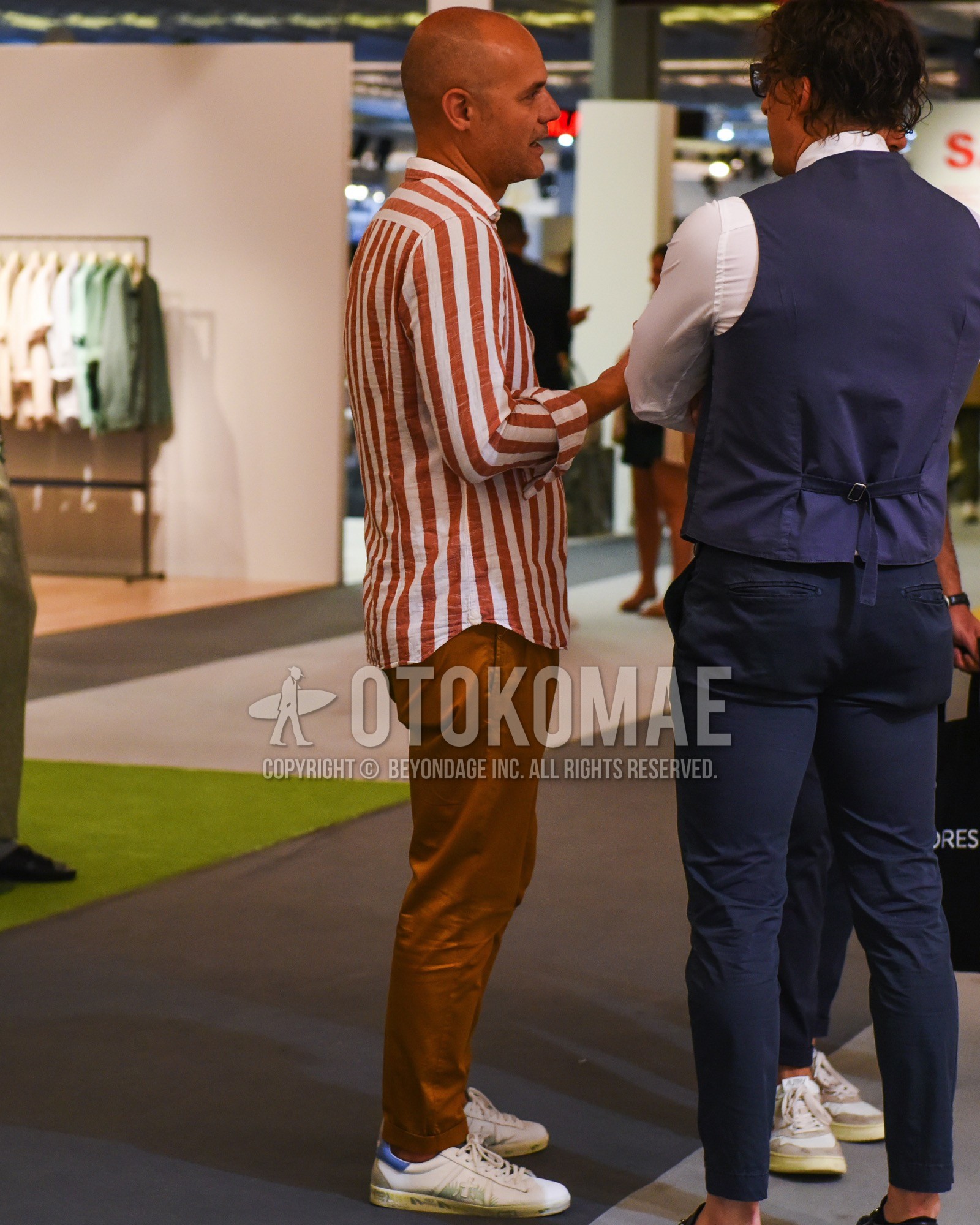 Men's spring summer outfit with red stripes shirt, brown plain chinos, white low-cut sneakers.