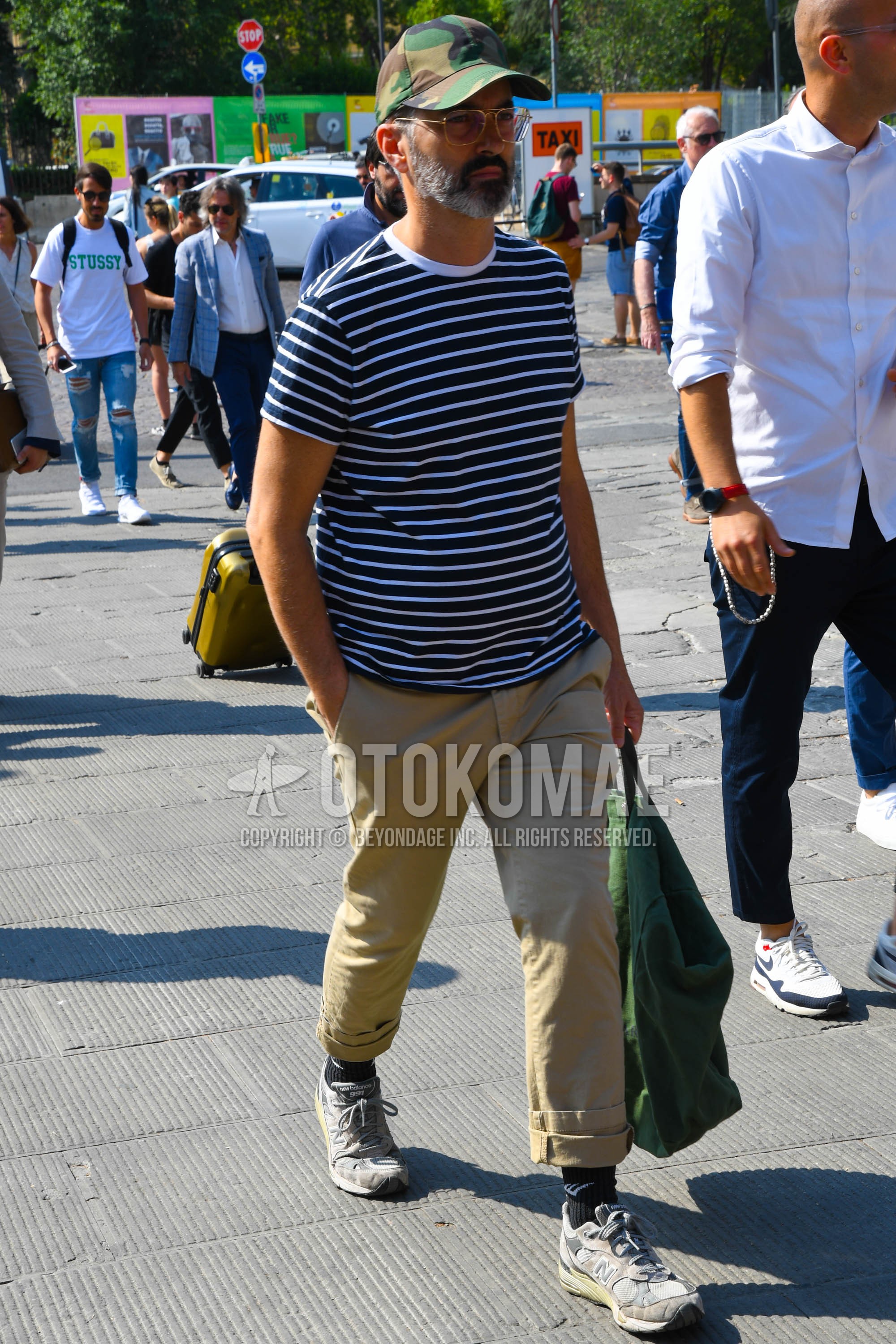 Men's summer outfit with camouflage baseball cap, white black horizontal stripes t-shirt, beige plain chinos, black one point socks, gray low-cut sneakers.