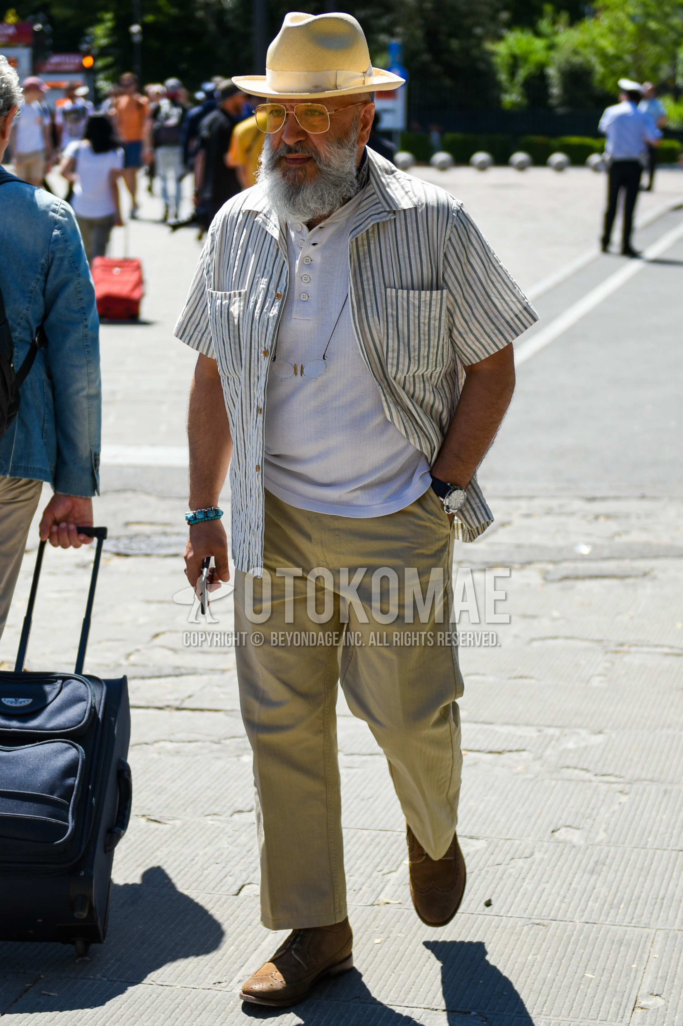 Men's spring summer outfit with beige plain hat, gold plain sunglasses, white stripes shirt jacket, white plain t-shirt, beige plain chinos, beige plain ankle pants, brown  boots.