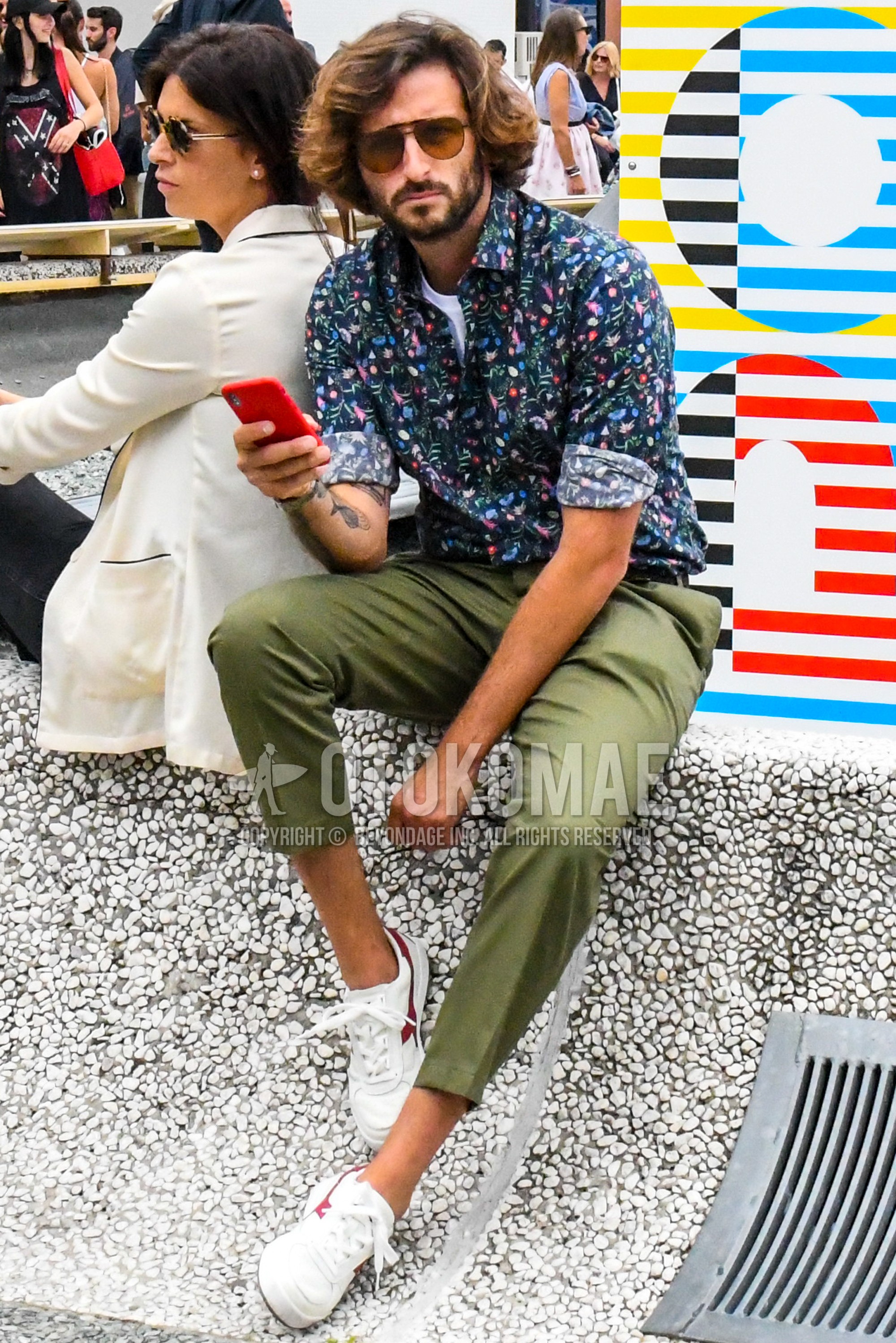 Men's spring summer outfit with plain sunglasses, navy botanical shirt, olive green plain ankle pants, olive green plain cotton pants, white low-cut sneakers.