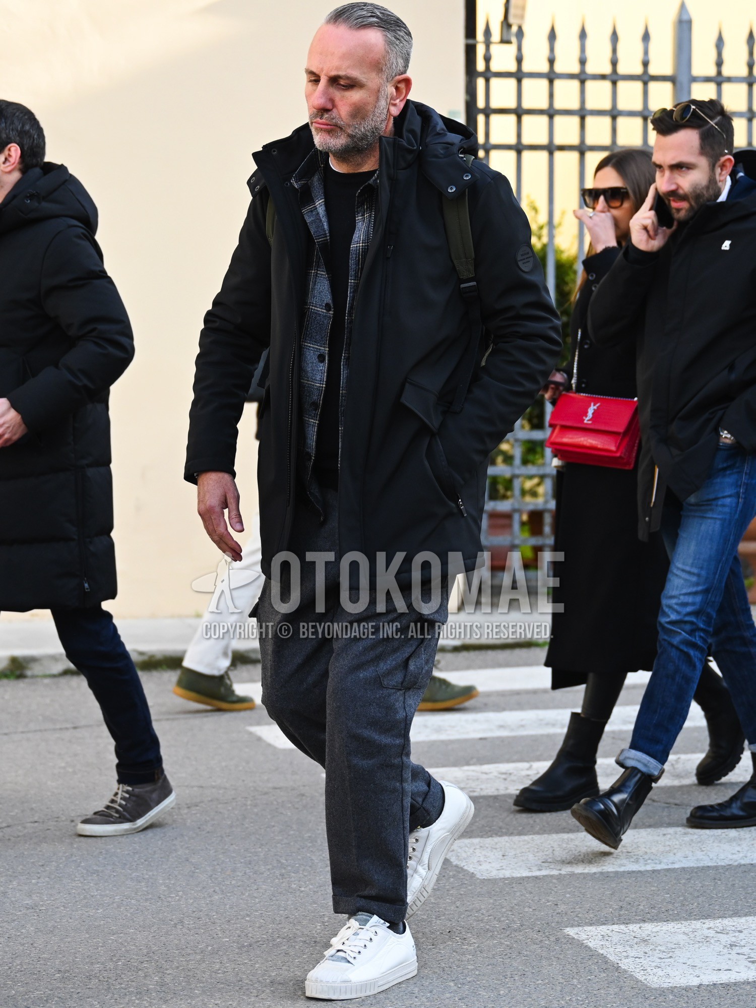 Men's autumn winter outfit with black plain hooded coat, navy check shirt, black plain long sleeve t-shirt, gray plain cargo pants, white low-cut sneakers, olive green plain backpack.
