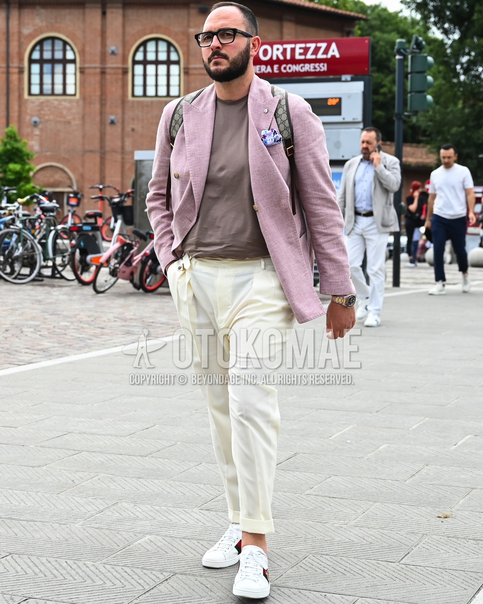 Men's spring summer autumn outfit with clear plain sunglasses, pink plain tailored jacket, beige plain t-shirt, white plain beltless pants, white low-cut sneakers, beige whole pattern backpack.