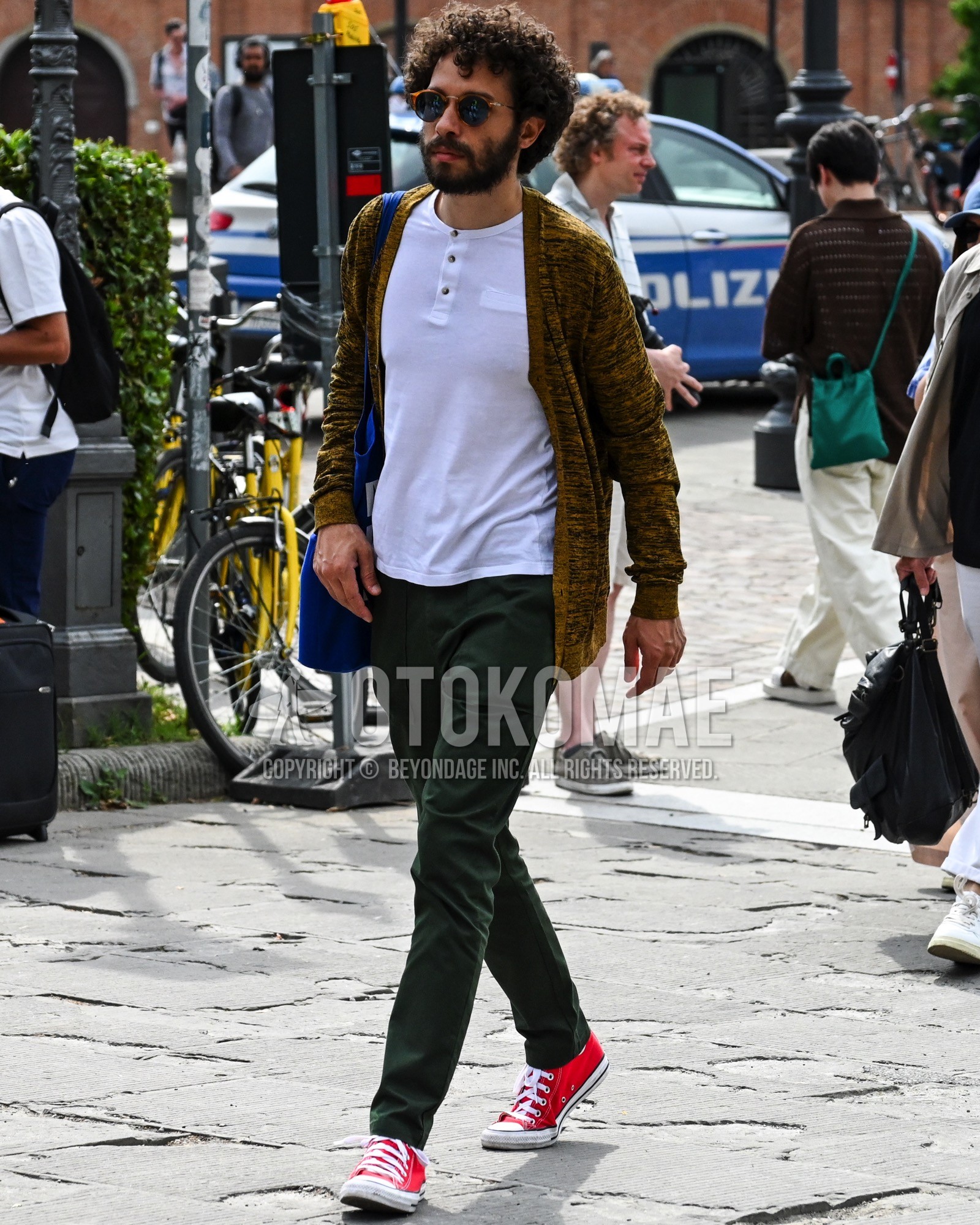 Men's spring summer autumn outfit with black plain sunglasses, white plain t-shirt, brown whole pattern cardigan, green plain chinos, red low-cut sneakers, navy plain tote bag.
