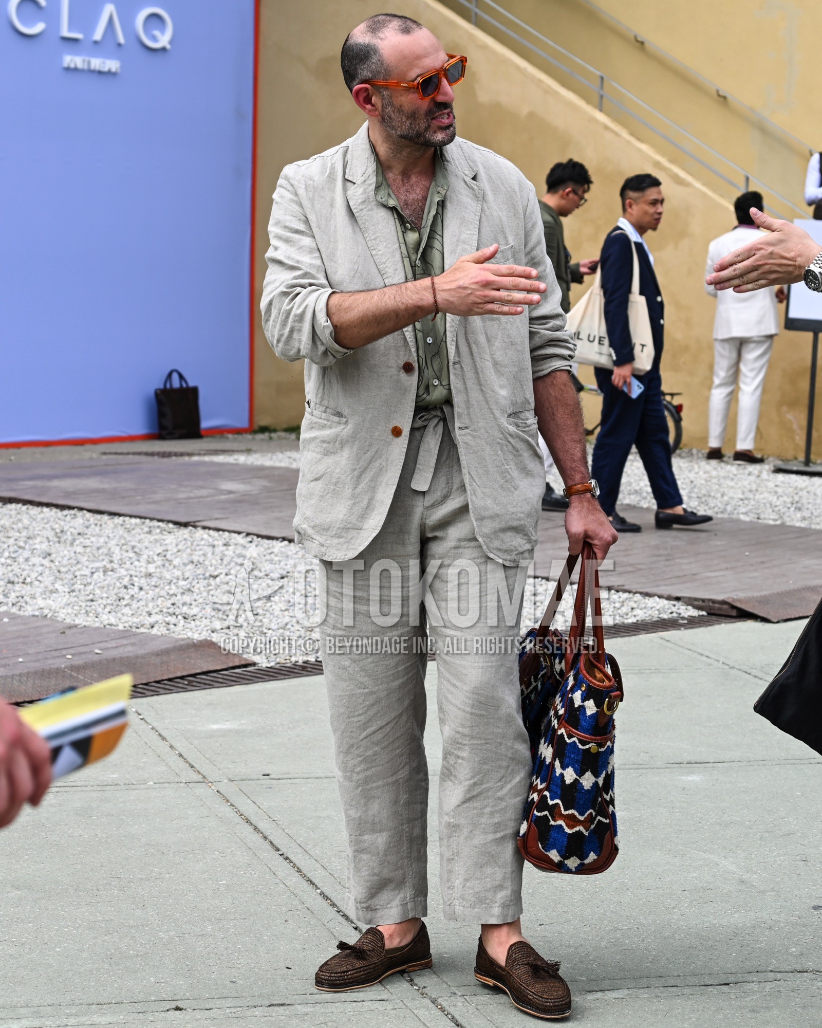 Men's spring summer autumn outfit with black plain sunglasses, green plain shirt, brown tassel loafers leather shoes, blue whole pattern tote bag, gray plain suit.