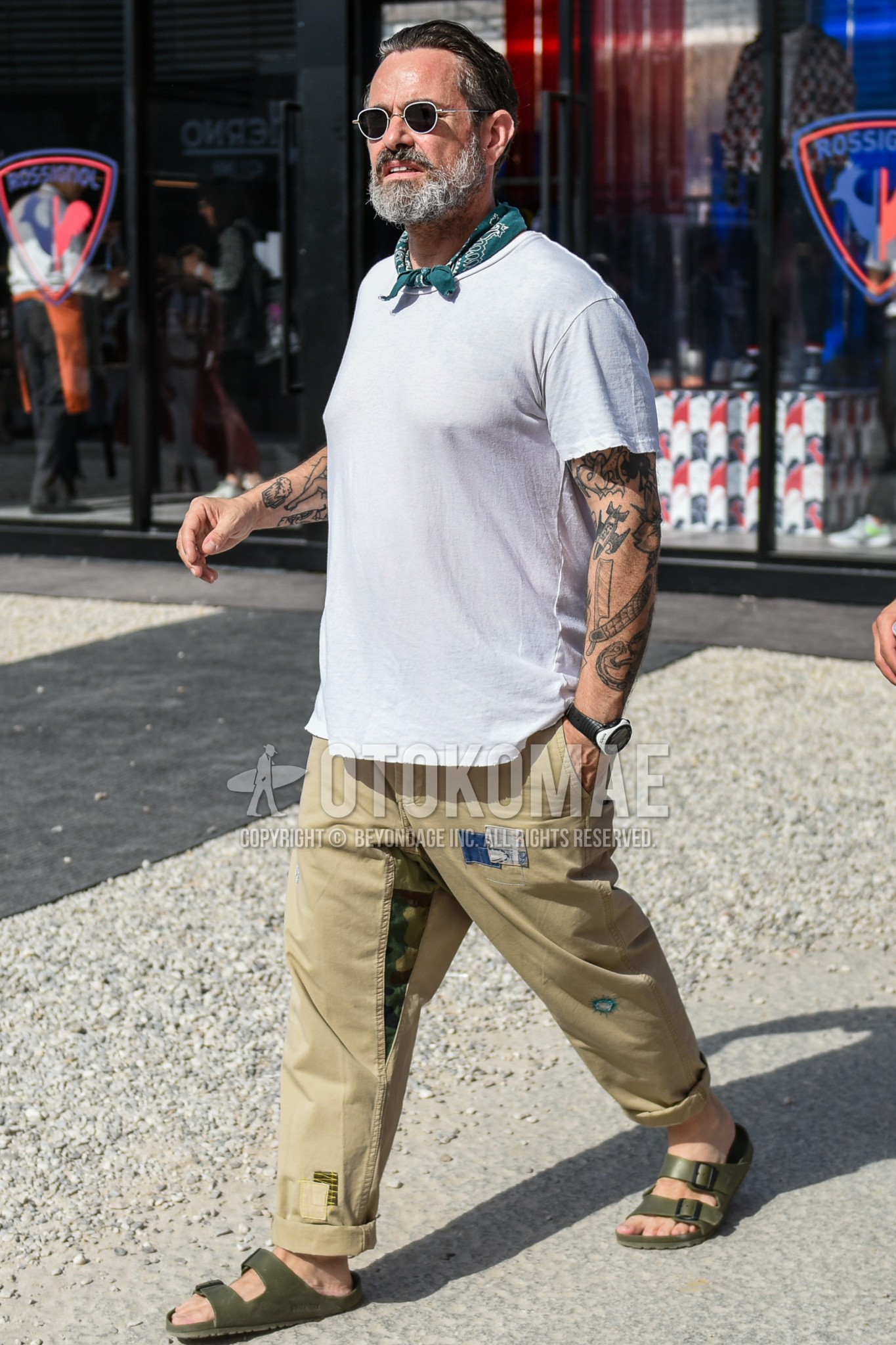 Men's summer outfit with plain sunglasses, green scarf bandana/neckerchief, white plain t-shirt, beige plain chinos, olive green leather sandals.