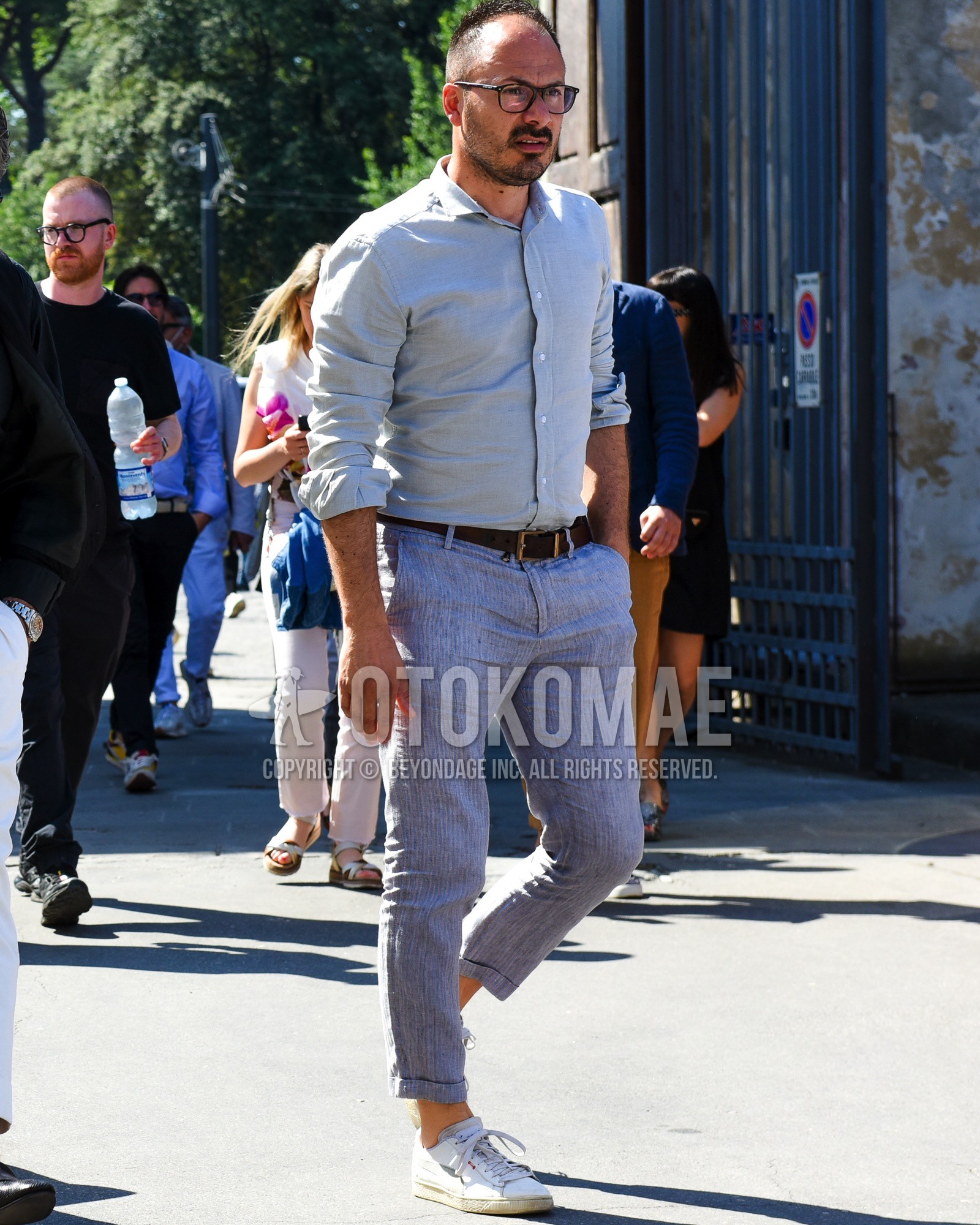 Men's spring summer outfit with brown tortoiseshell glasses, gray plain shirt, brown plain leather belt, blue stripes chinos, white low-cut sneakers.