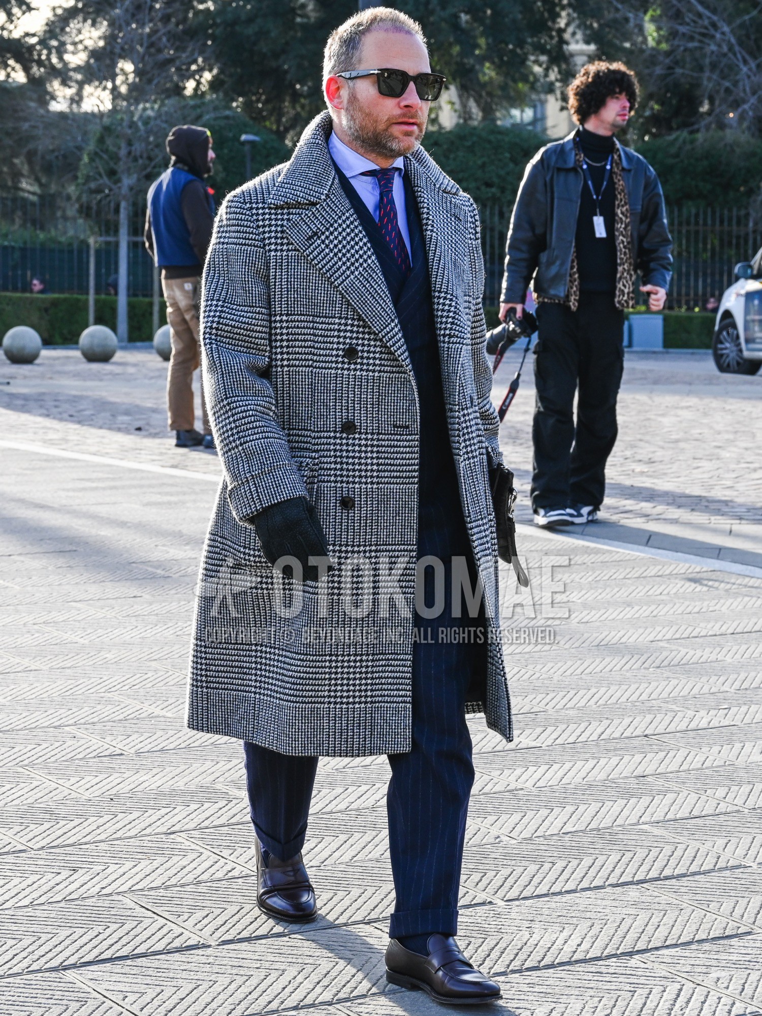 Men's autumn winter outfit with black plain sunglasses, gray check ulster coat, blue plain shirt, navy plain socks, brown coin loafers leather shoes, navy stripes suit, navy graphic necktie.