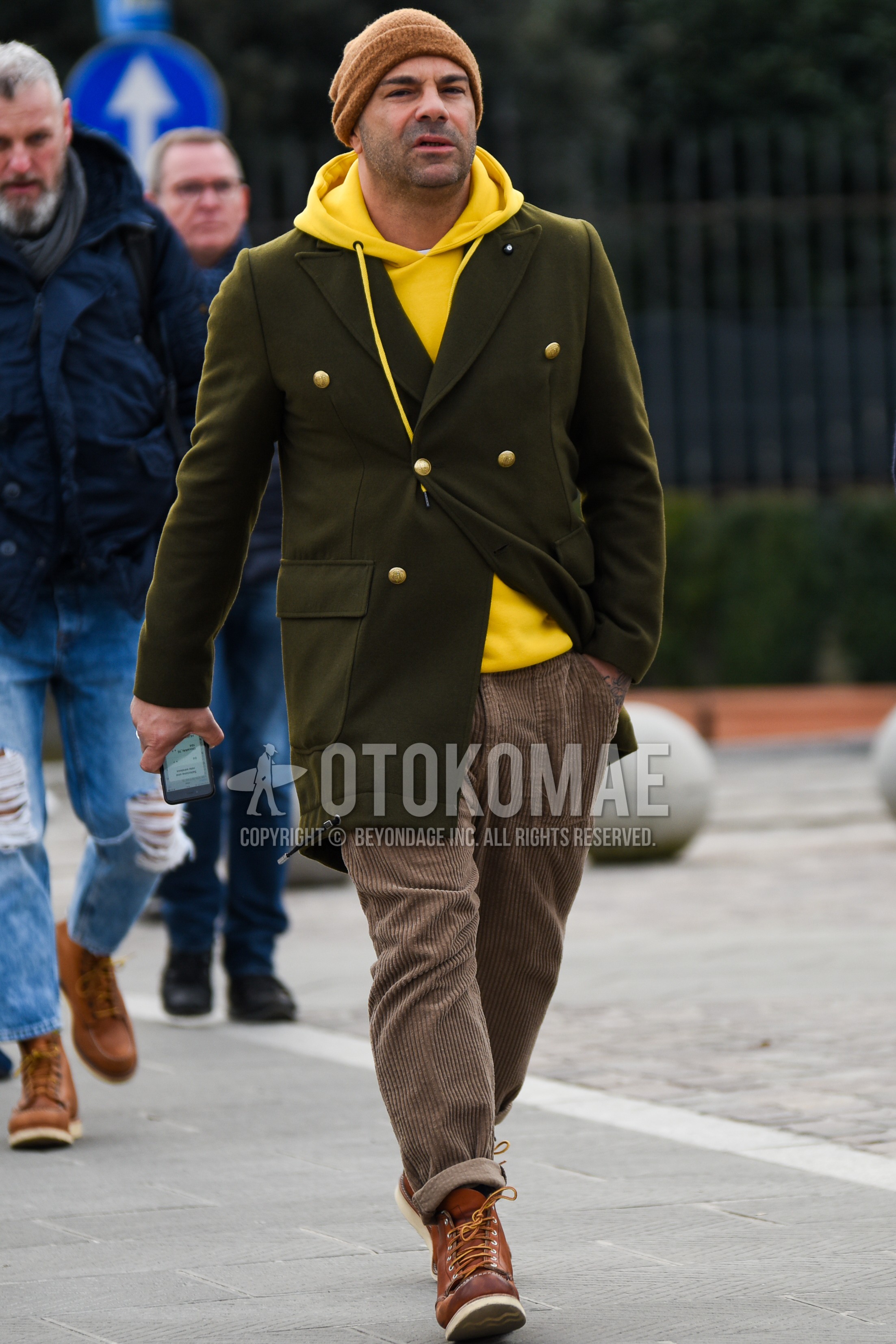 Men's autumn winter outfit with brown plain knit cap, olive green plain chester coat, yellow plain hoodie, brown plain winter pants (corduroy,velour), brown work boots.