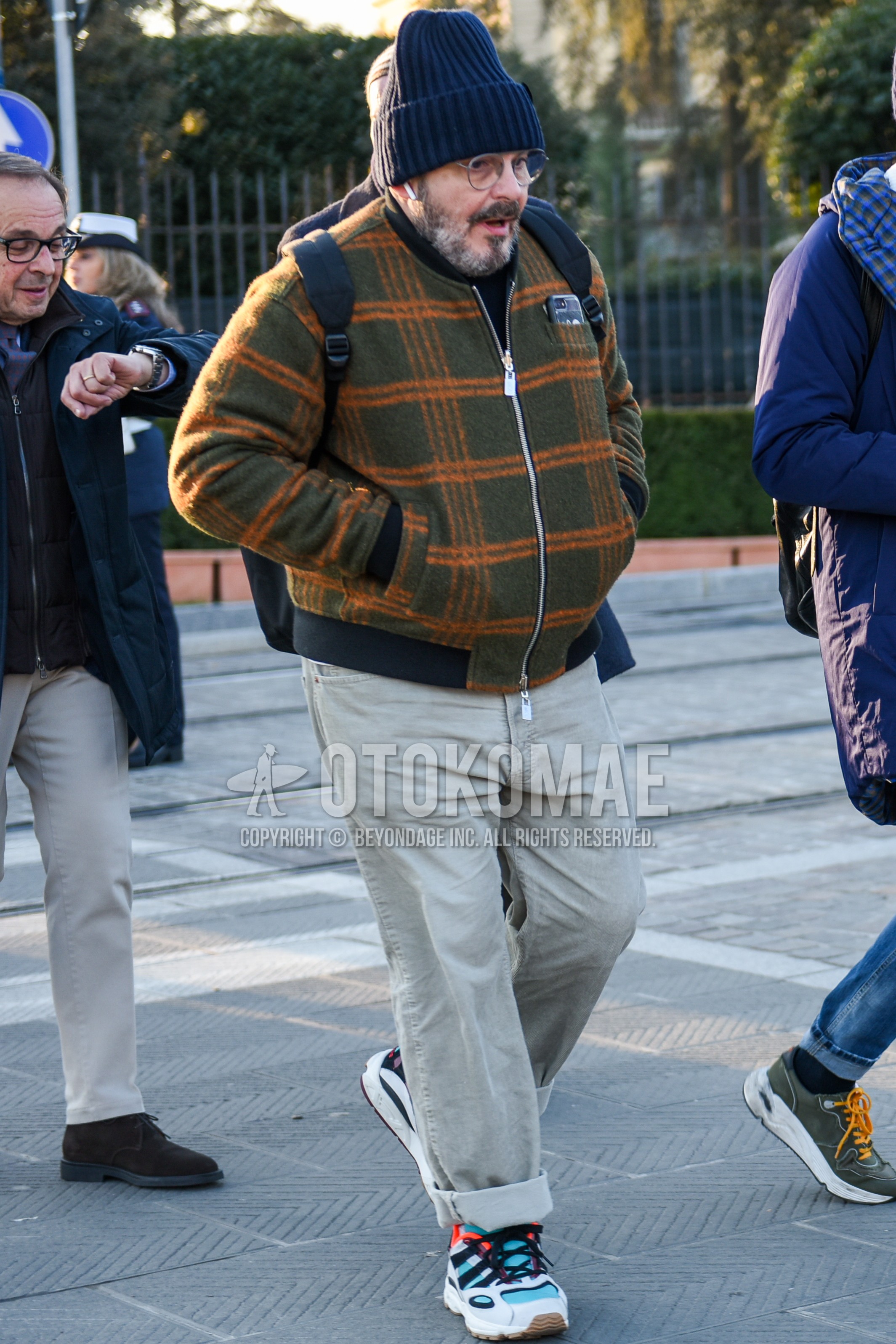 Men's autumn winter outfit with navy plain knit cap, silver plain glasses, olive green orange check MA-1, beige plain chinos, multi-color low-cut sneakers, black plain backpack.