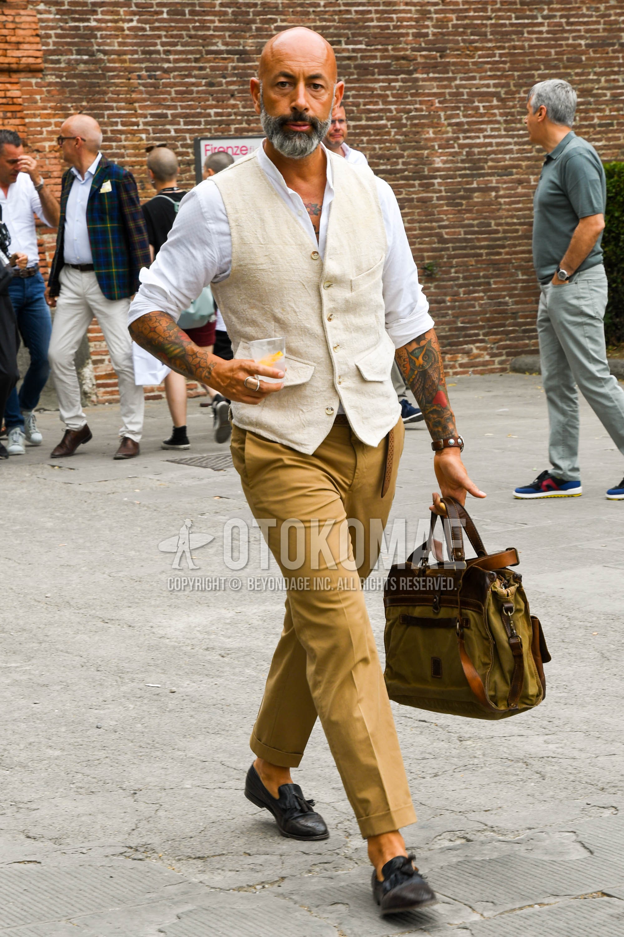 Men's spring summer autumn outfit with beige plain gilet, white plain shirt, beige plain chinos, brown tassel loafers leather shoes, olive green plain briefcase/handbag.