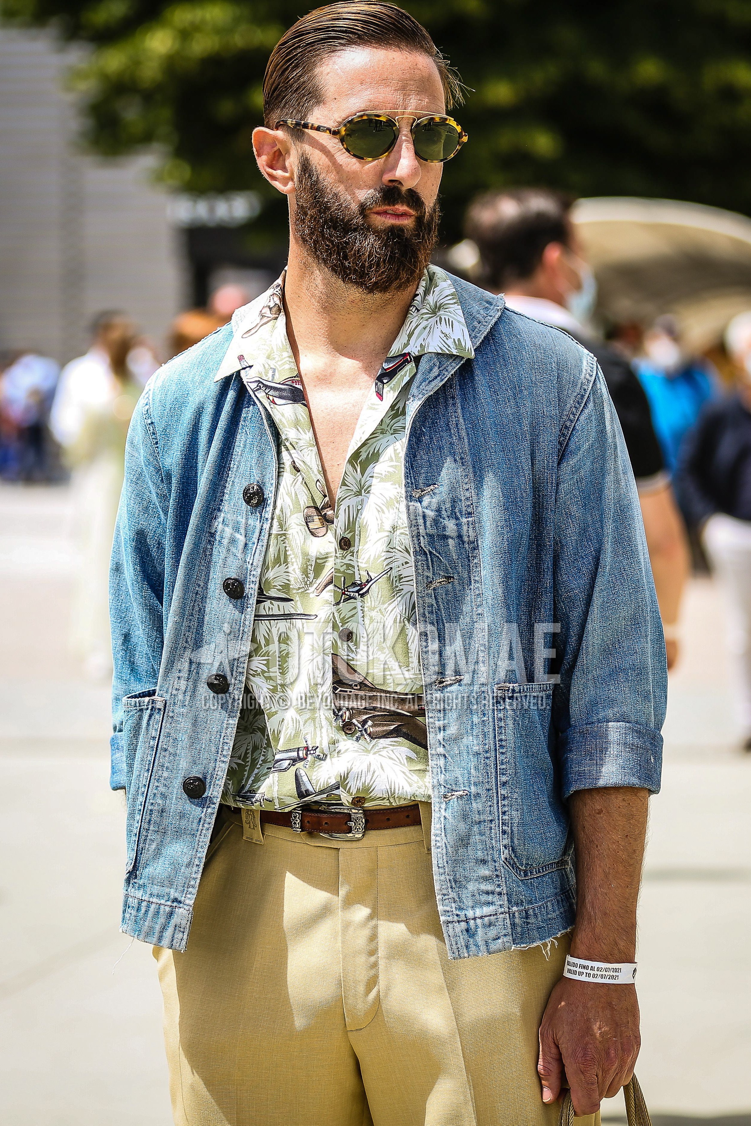 Men's spring summer outfit with yellow brown tortoiseshell sunglasses, blue plain denim jacket, olive green botanical shirt, brown plain leather belt, yellow beige plain slacks.