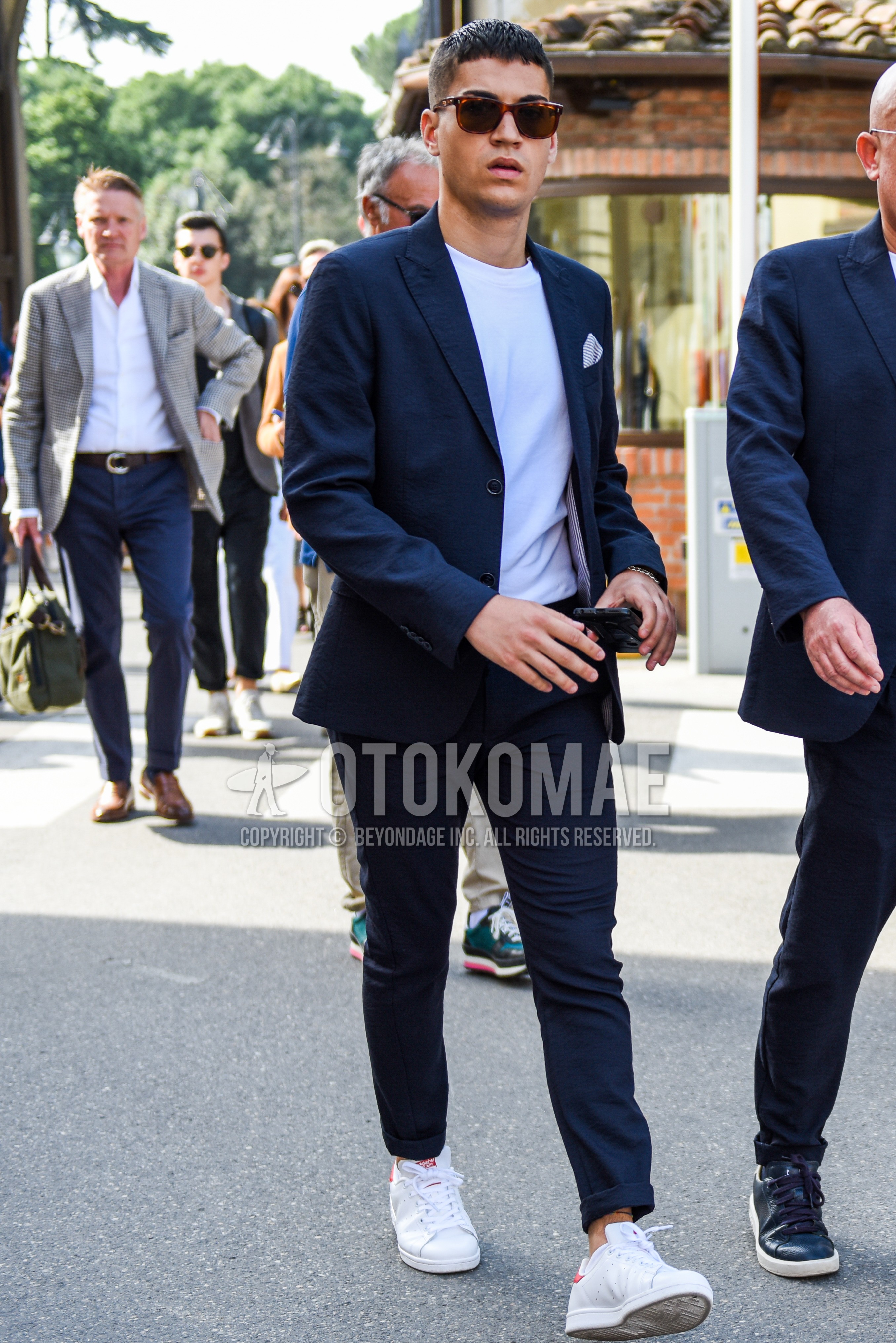 Men's spring summer autumn outfit with brown tortoiseshell sunglasses, white plain t-shirt, white low-cut sneakers, navy plain suit.