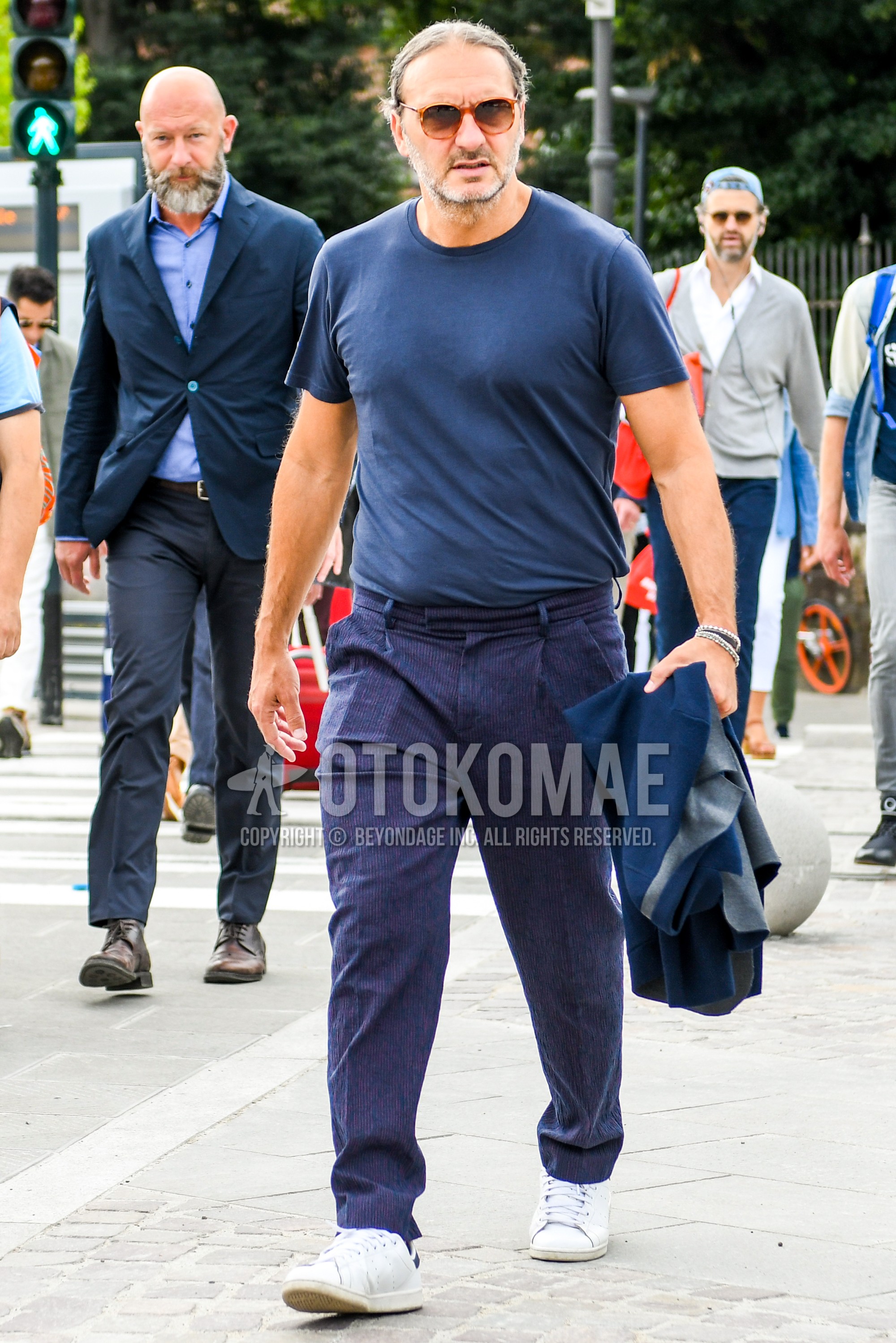 Men's summer outfit with plain sunglasses, blue plain t-shirt, navy plain pleated pants, white low-cut sneakers.