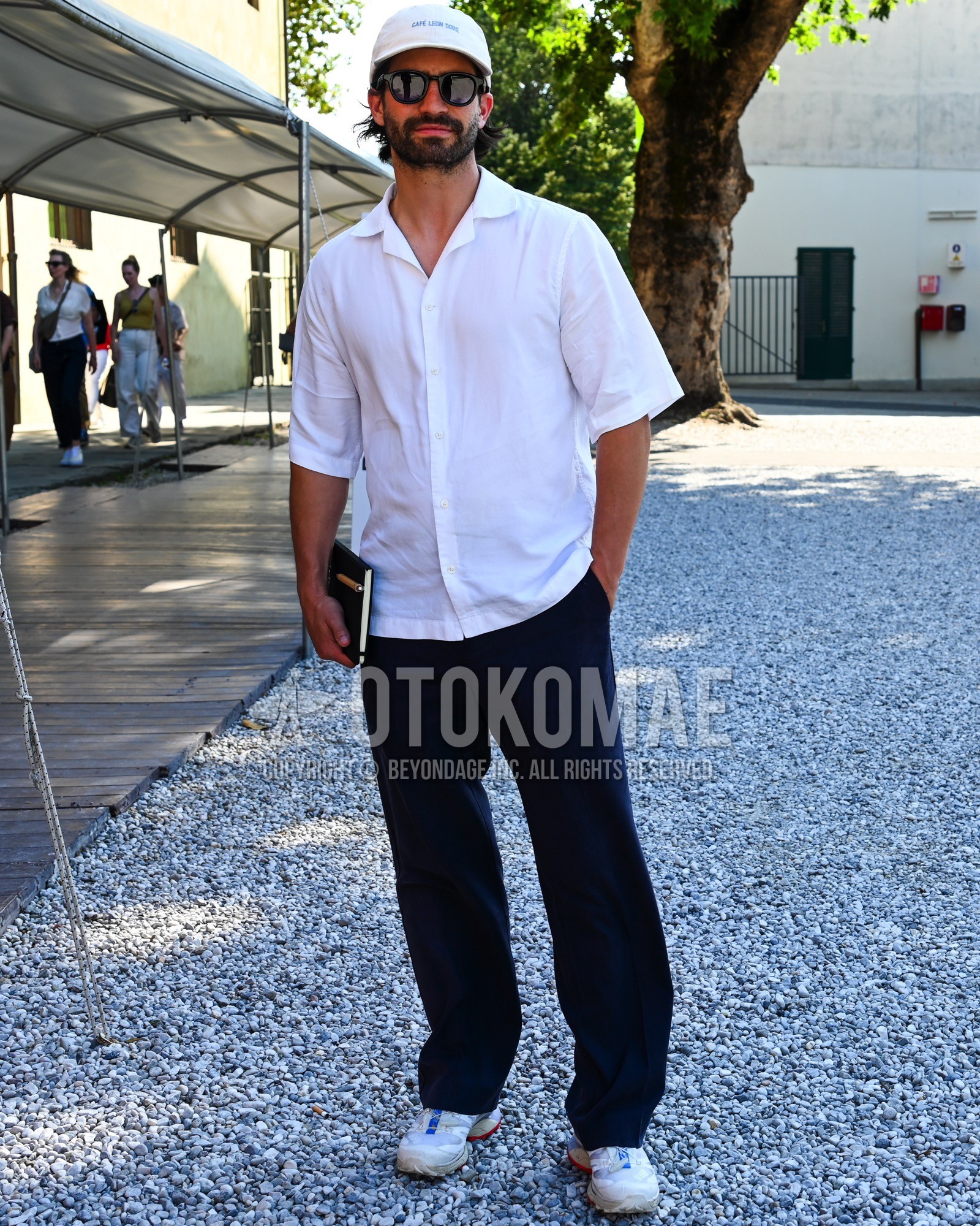 Men's spring summer outfit with white one point baseball cap, black plain sunglasses, white plain shirt, black plain slacks, white low-cut sneakers.