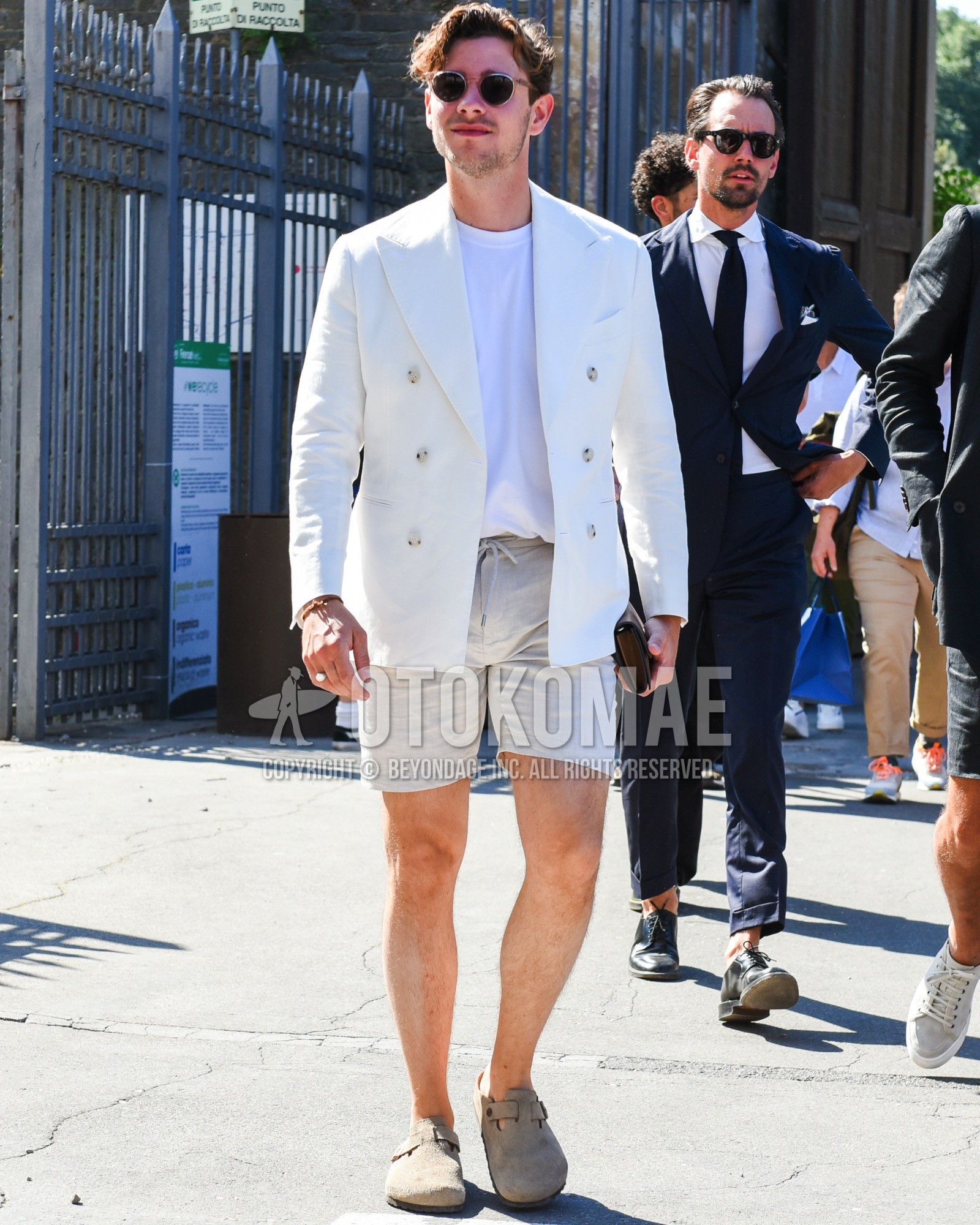 Men's spring summer outfit with silver brown plain sunglasses, white plain tailored jacket, white plain t-shirt, white plain easy pants, white plain short pants, beige leather sandals.