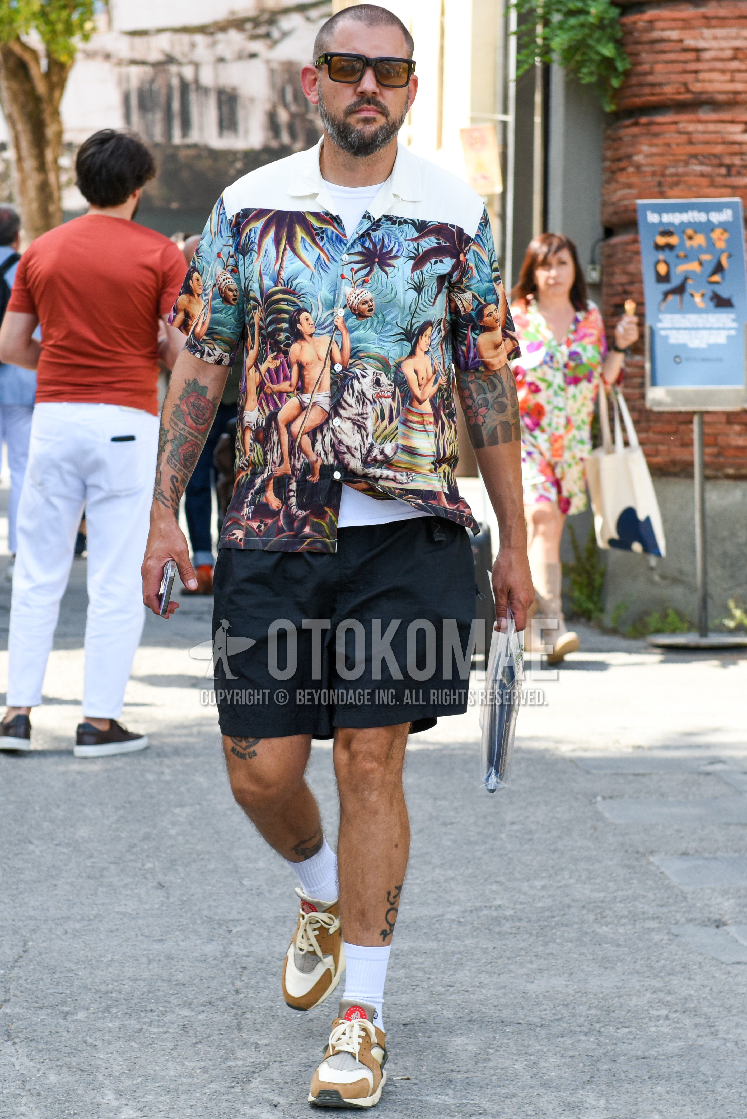 Men's spring summer outfit with black plain sunglasses, blue white graphic shirt, white plain t-shirt, black plain short pants, white plain socks, brown low-cut sneakers.