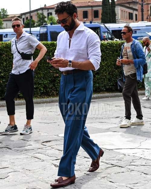 黒無地のサングラス、白無地のシャツ、黒無地のレザーベルト、ブルー無地のプリーツパンツ、ブルー無地のスラックス、ブラウンタッセルローファーの革靴を合わせた春夏秋のメンズコーデ・着こなし。