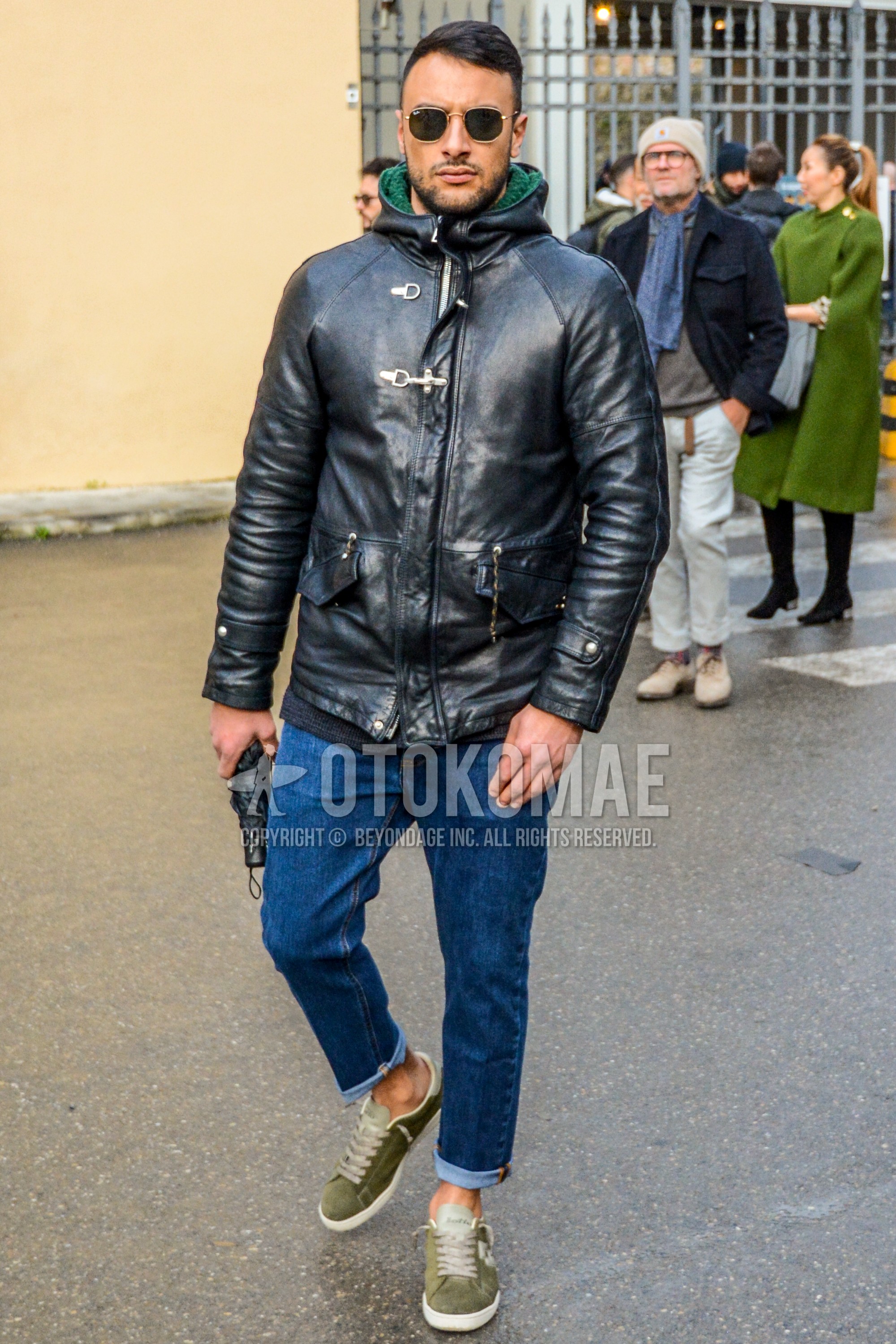 Men's winter outfit with plain sunglasses, black plain leather jacket, blue plain denim/jeans, olive green low-cut sneakers.