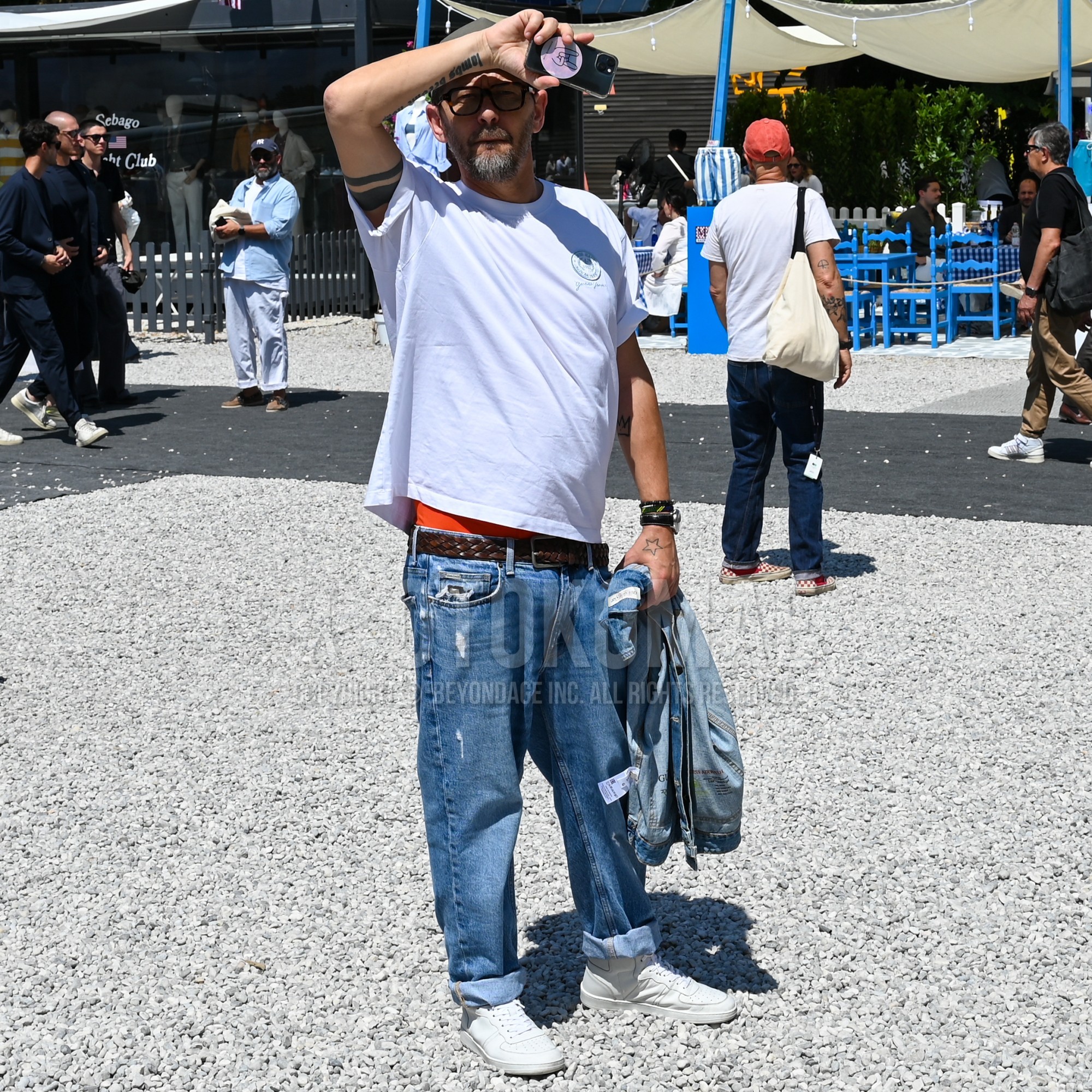 ブラウンべっ甲のメガネ、ブルー無地のデニムジャケット、白ワンポイントのTシャツ、ブラウン無地のメッシュベルト、ブラウン無地のレザーベルト、ブルー無地のダメージジーンズ、白ローカットのスニーカーを合わせた春夏のメンズコーデ・着こなし。