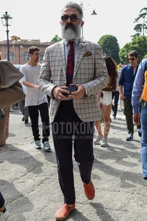 黒無地のサングラス、ベージュチェックのテーラードジャケット、白無地のシャツ、ネイビー無地のコットンパンツ、オレンジスリッポンのスニーカー、レッドネクタイのネクタイを合わせた春秋のメンズコーデ・着こなし。