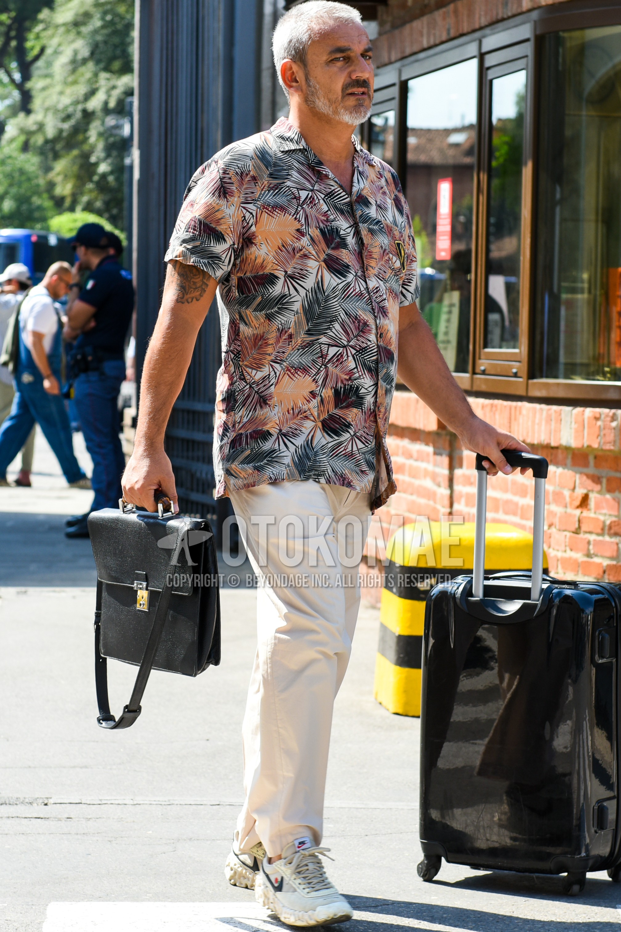 Men's spring summer outfit with multi-color botanical shirt, white plain chinos, black plain briefcase/handbag, black plain suitcase.