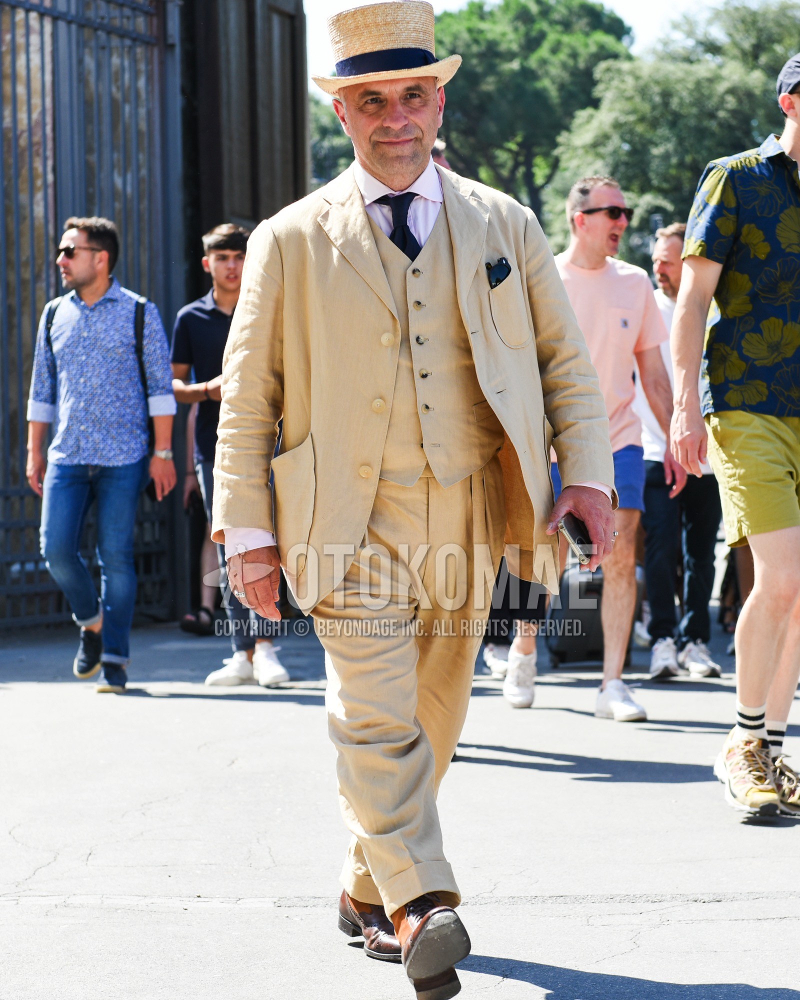 Men's spring summer outfit with beige plain hat, graphic shirt, brown straight-tip shoes leather shoes, beige plain three-piece suit, black plain necktie.