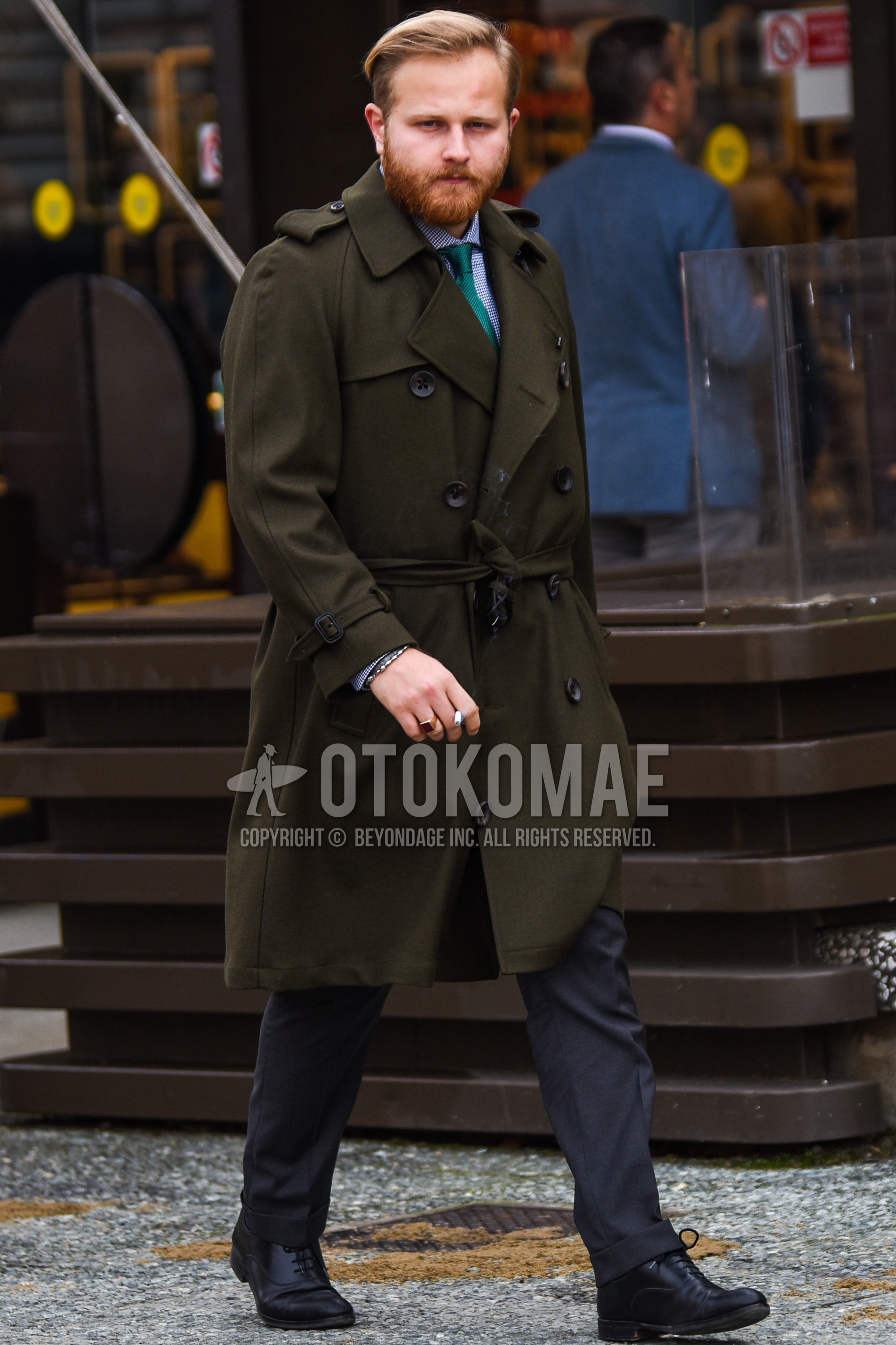 Men's winter outfit with olive green plain trench coat, blue check shirt, gray plain slacks, black straight-tip shoes leather shoes, green plain necktie.