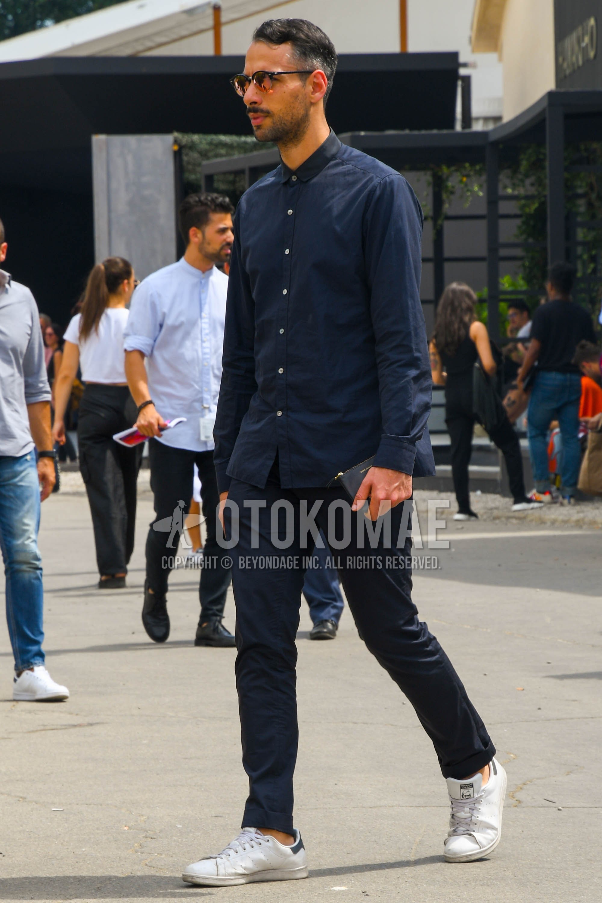Men's spring summer outfit with black plain sunglasses, black plain shirt, black plain chinos, white low-cut sneakers.