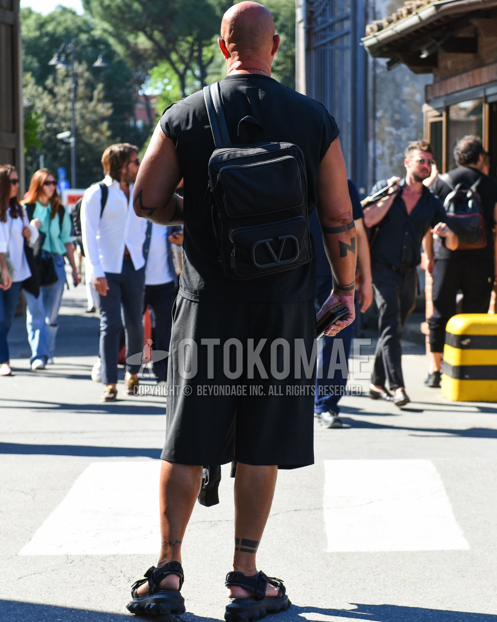 Men's spring summer outfit with black plain t-shirt, black plain short pants, black sport sandals, black plain backpack.