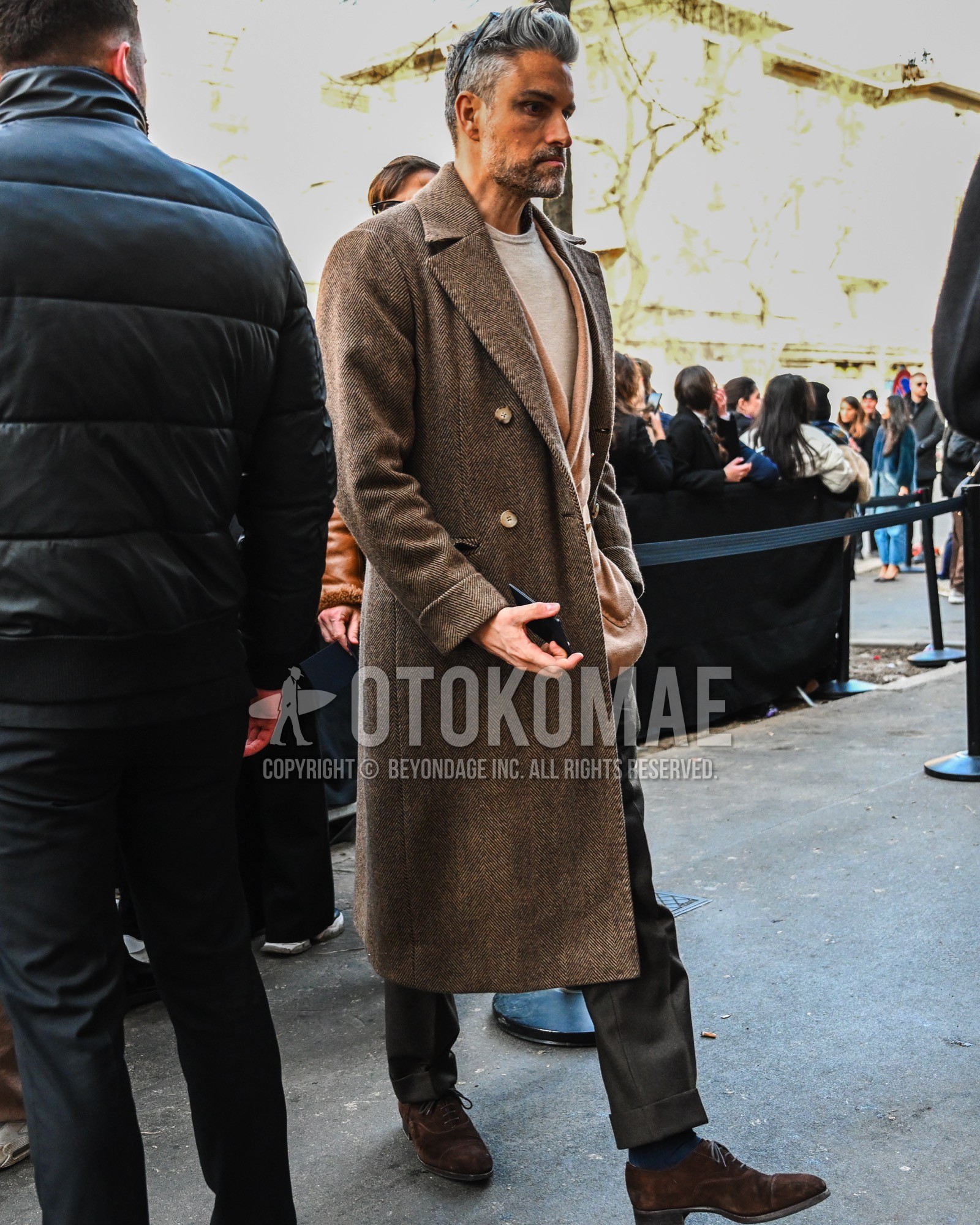 Men's autumn winter outfit with brown herringbone chester coat, brown plain tailored jacket, beige plain sweater, gray plain slacks, navy plain socks, brown straight-tip shoes leather shoes.