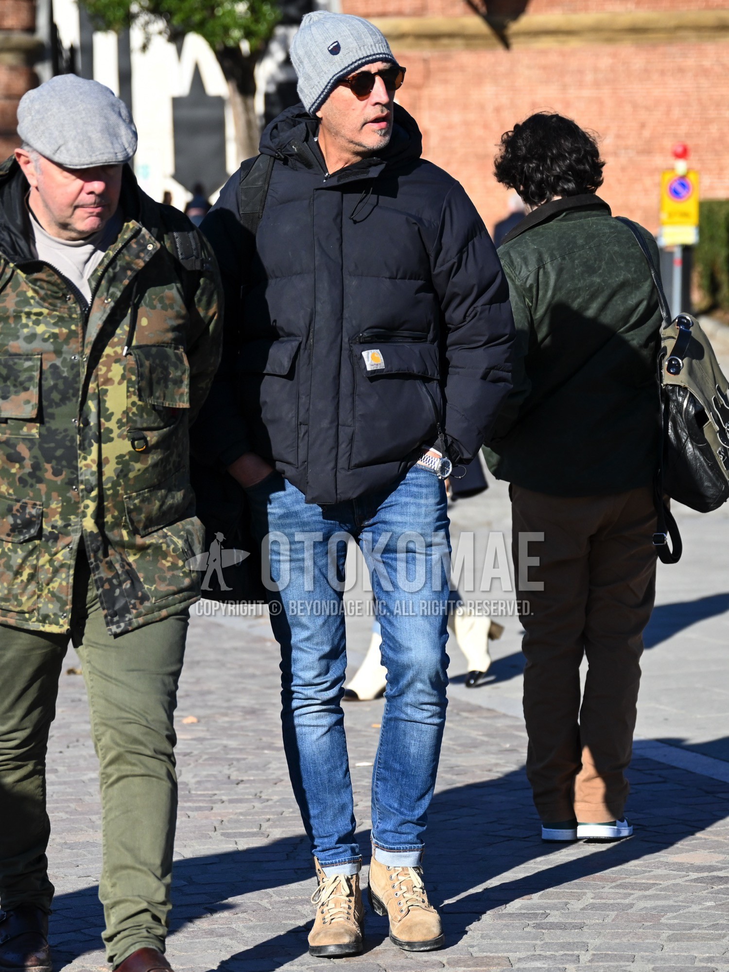 Men's autumn winter outfit with gray plain knit cap, brown tortoiseshell sunglasses, black plain down jacket, black plain hooded coat, blue plain denim/jeans, beige work boots.