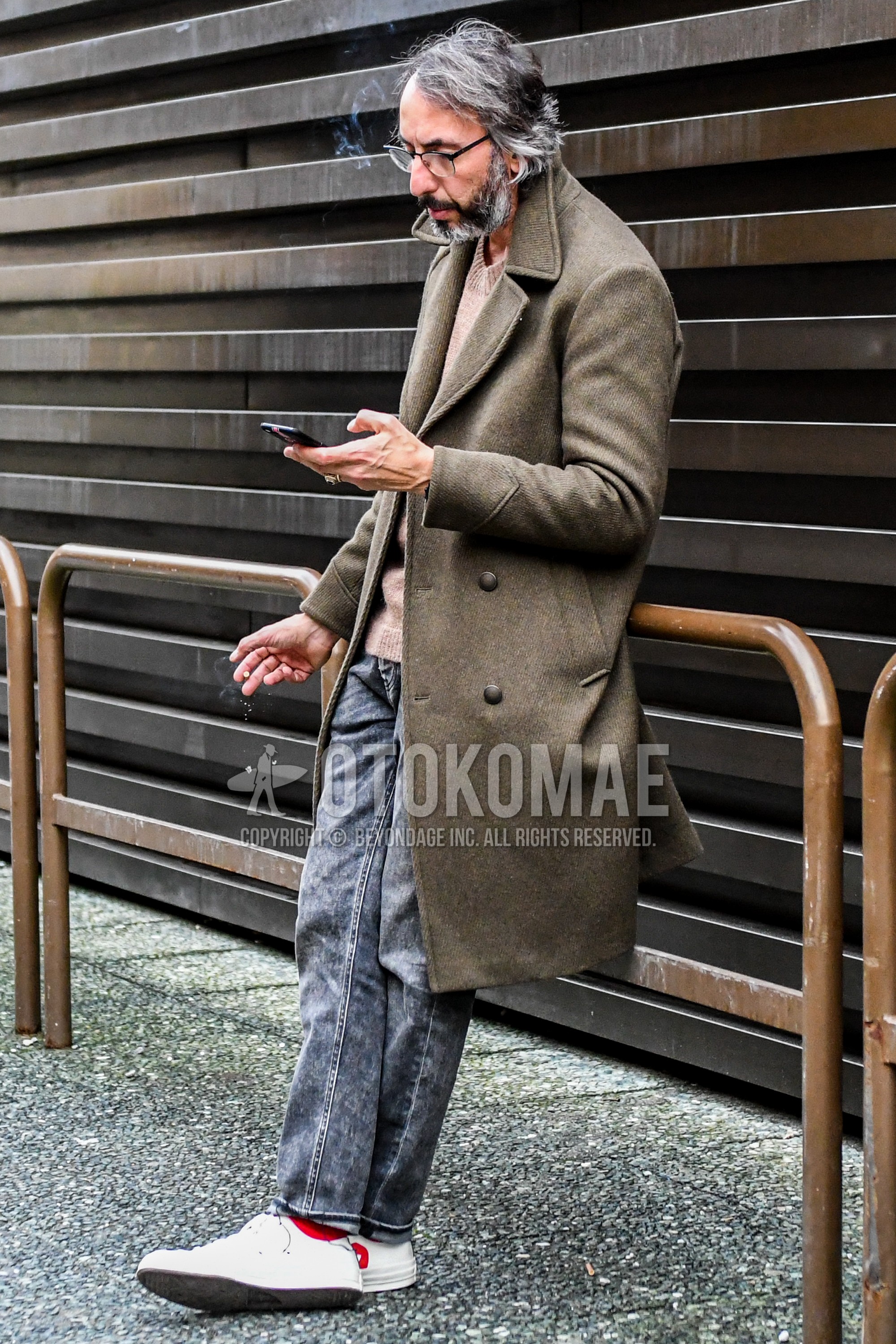 Men's winter outfit with brown plain ulster coat, beige plain sweater, gray plain denim/jeans, red plain socks, white low-cut sneakers.
