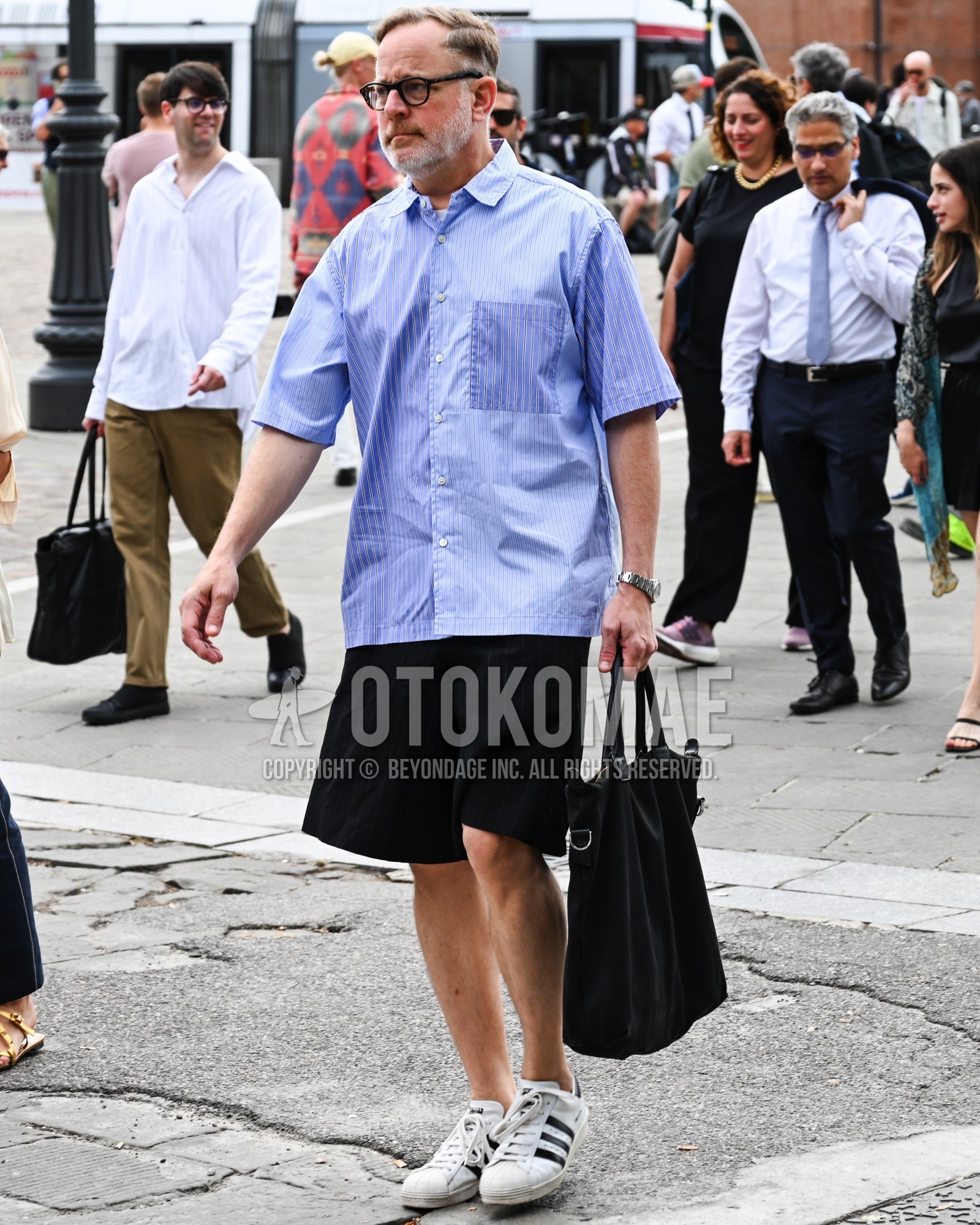 Men's spring summer outfit with clear plain sunglasses, light blue stripes shirt, black plain short pants, white low-cut sneakers, black plain tote bag.
