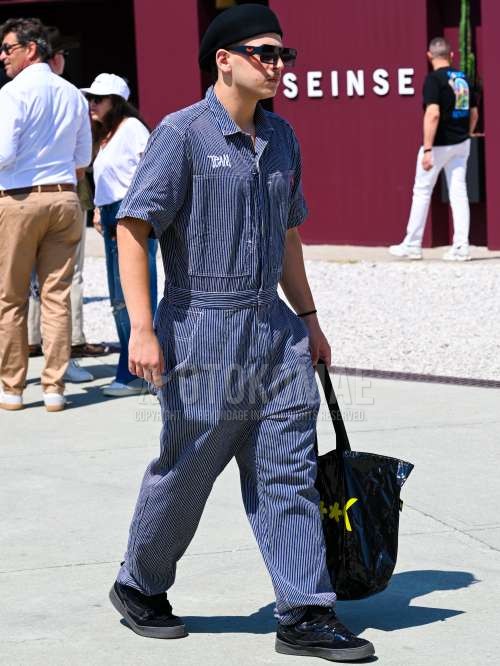 黒無地のキャップ、プラダのブラウン・ブルーべっ甲のサングラス、ブルーストライプのジャンプスーツ、ブルー・黒ローカットのスニーカー、黒レタードのトートバッグを合わせた夏春のメンズコーデ・着こなし。